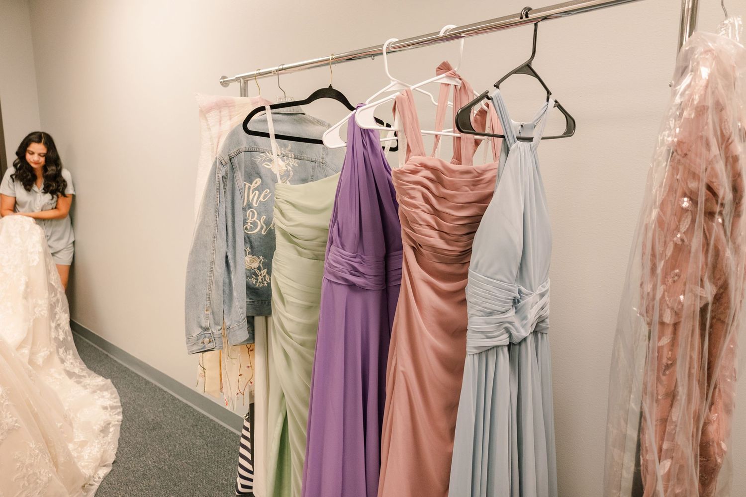 Colorful bridesmaid dresses in pastels and blush tones hanging on a rack in a bridal shop.