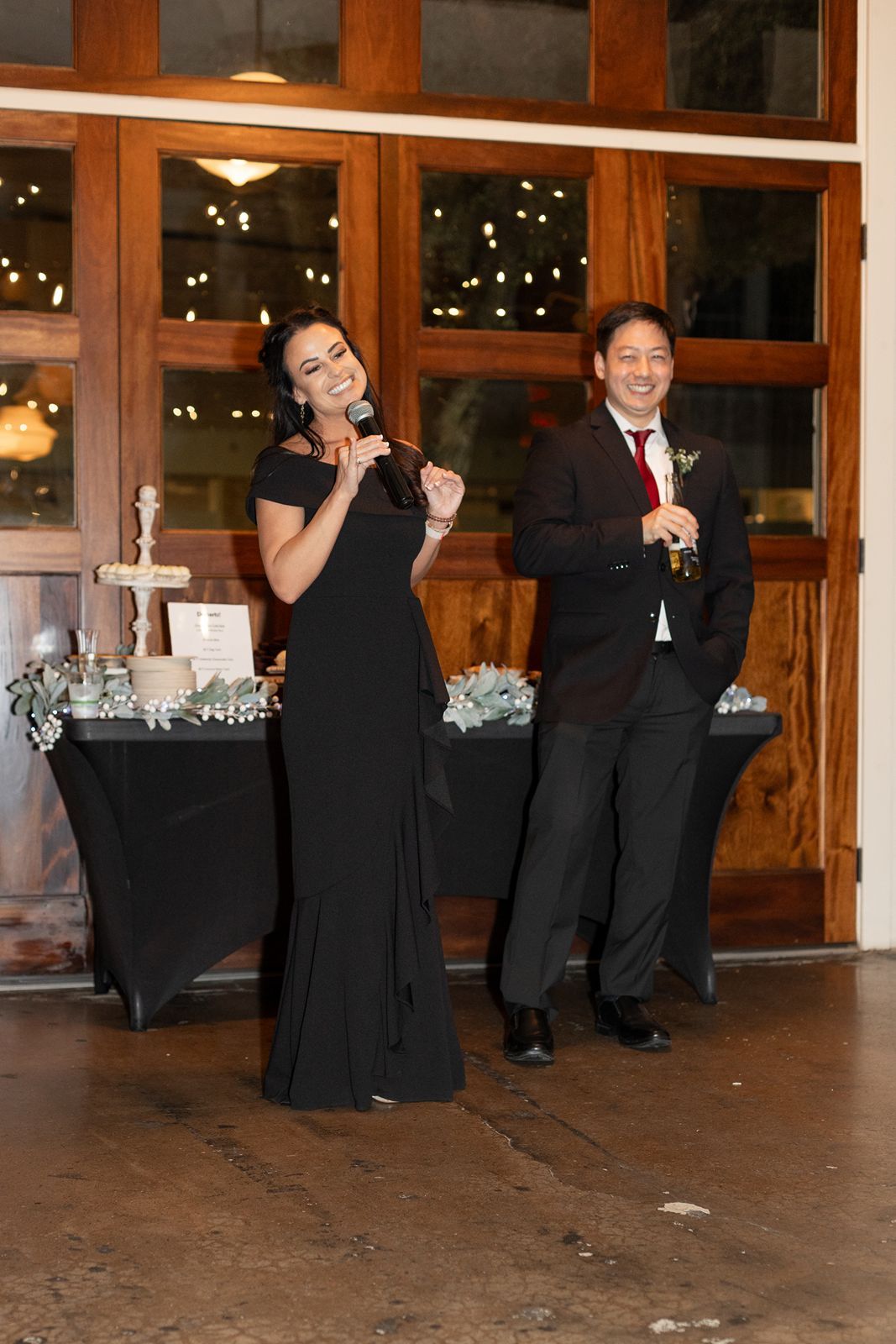 Wedding party members in formal black attire perform synchronized dance moves at an indoor reception venue.