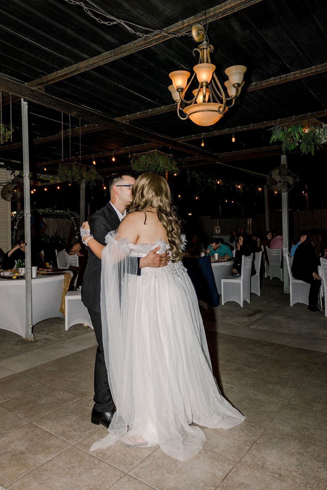 Bride and groom share their first dance under a chandelier at an elegant outdoor wedding reception.