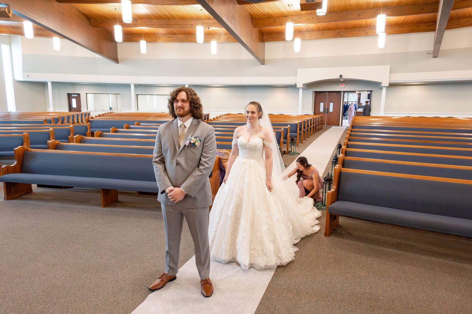 Wedding party members walk together through a church hallway with wooden beams and blue pews.