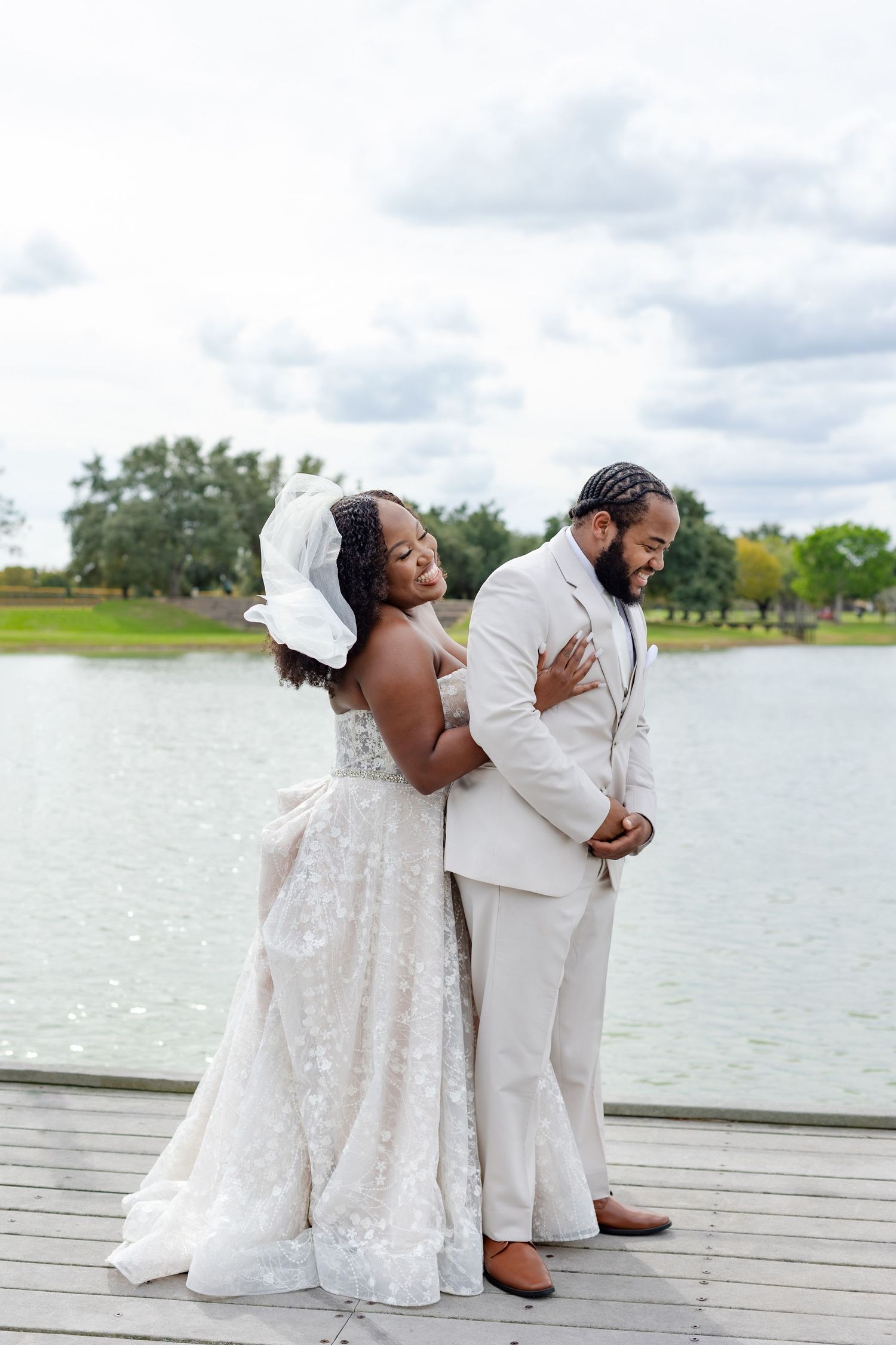 Wedding couple poses for romantic photos on a lakeside deck in white formal attire.