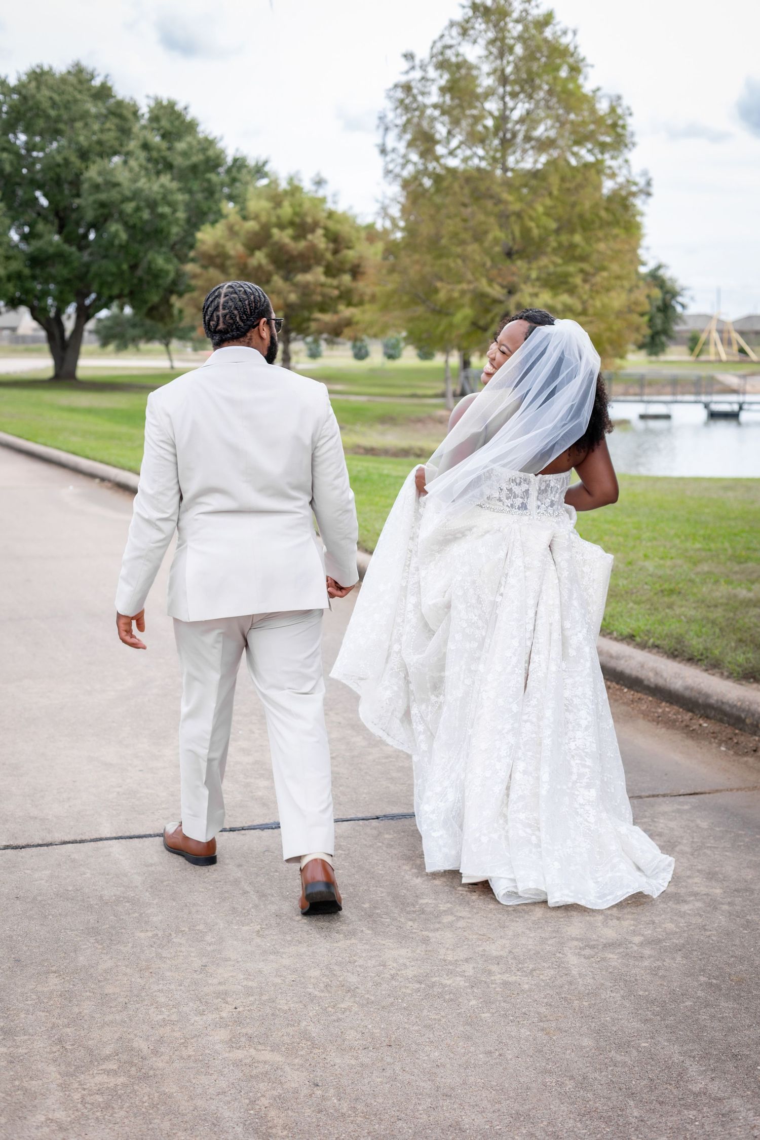 Wedding couple walking together on pathway with bride's white lace dress trailing behind.
