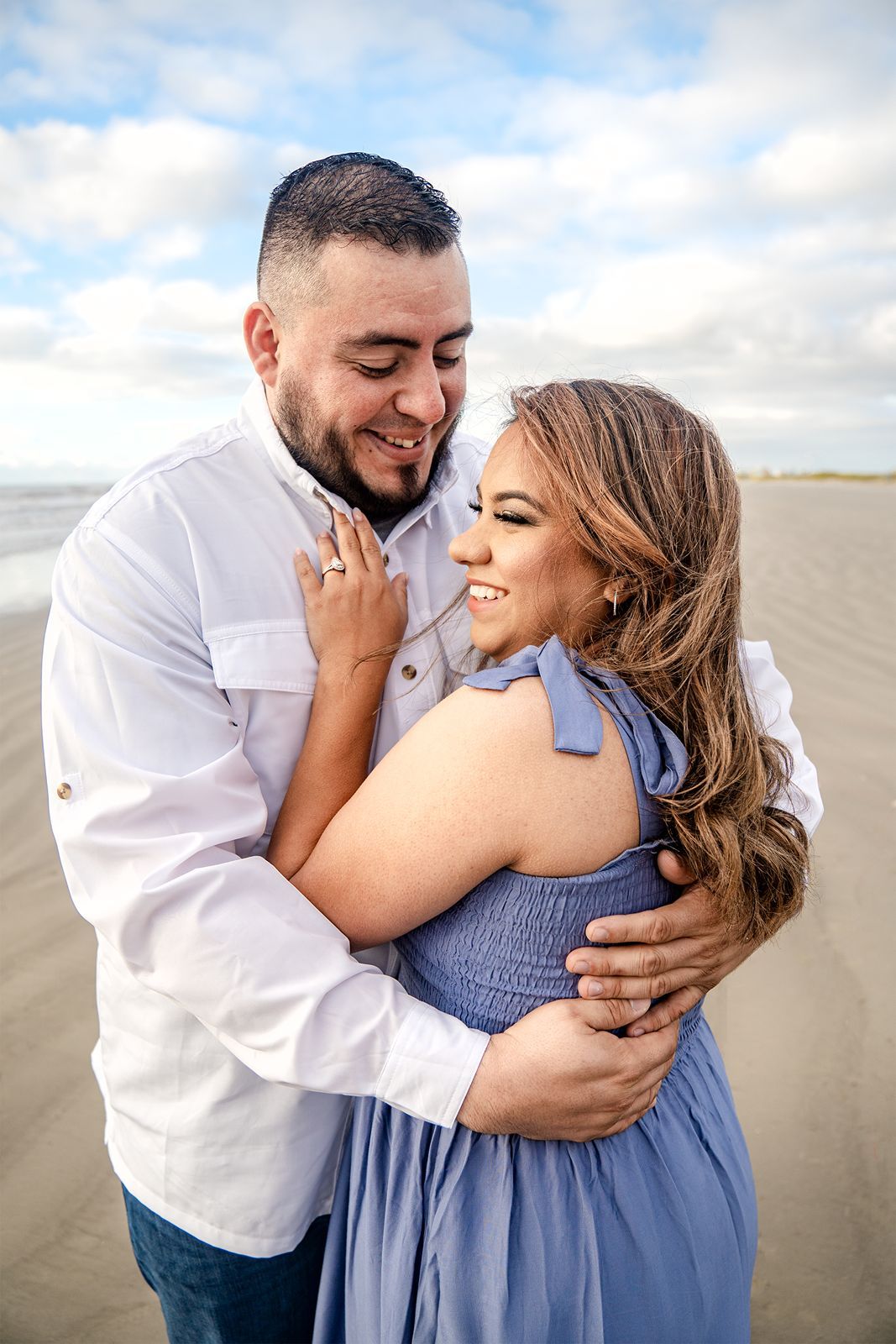 A couple in white and blue outfits share intimate moments on a cloudy beach in a series of romantic photos.