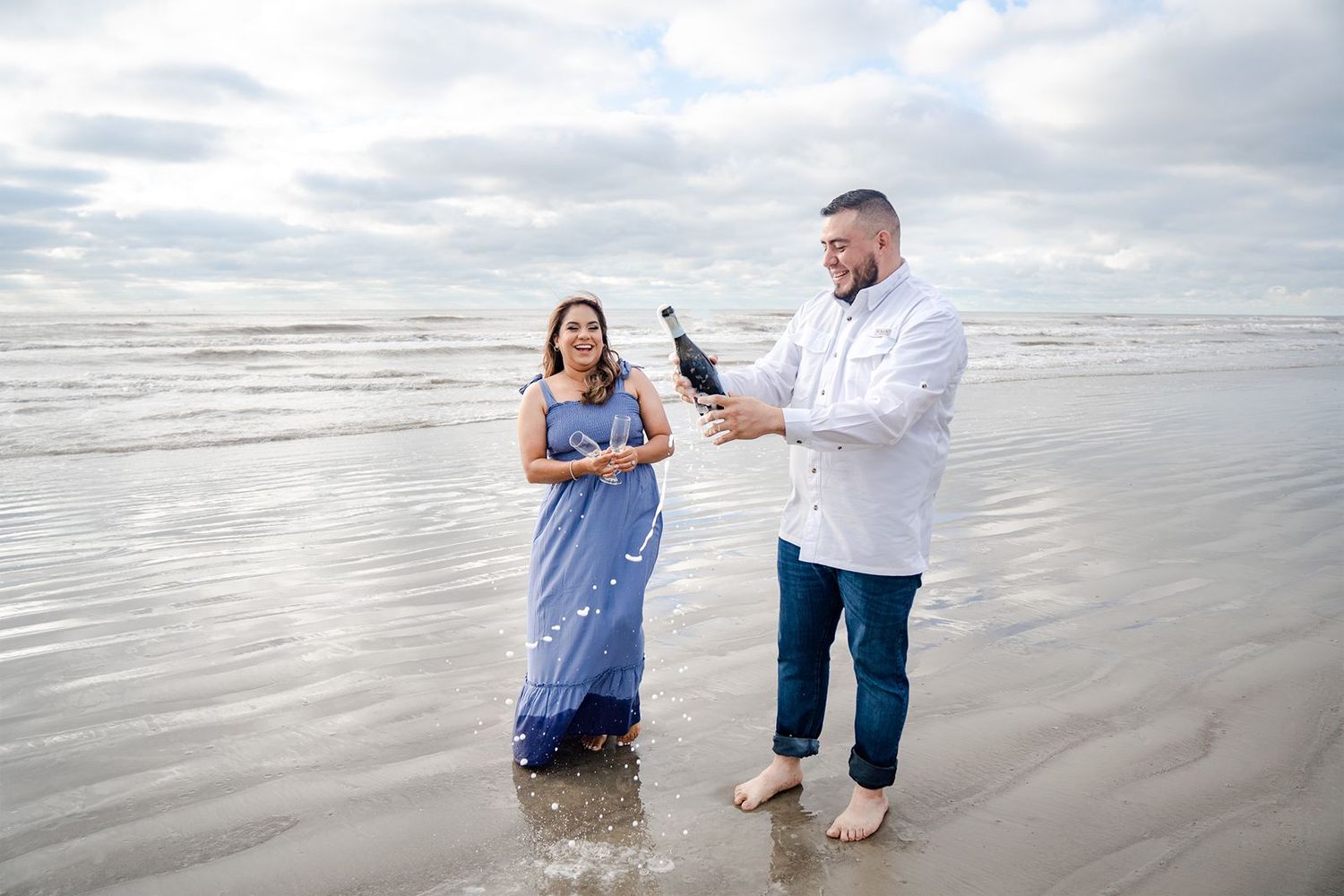 A couple splashes and plays together in the ocean waves on a cloudy day at the beach.
