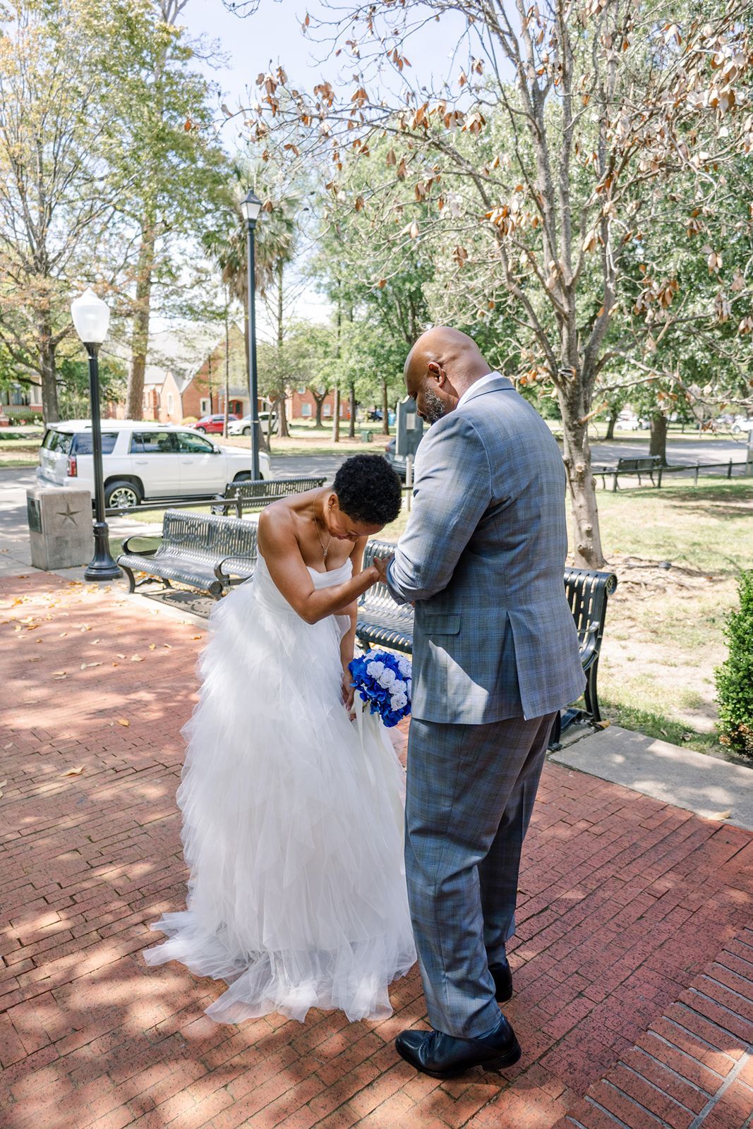 Groom in gray plaid suit embraces bride in white ruffled gown during outdoor wedding first look.