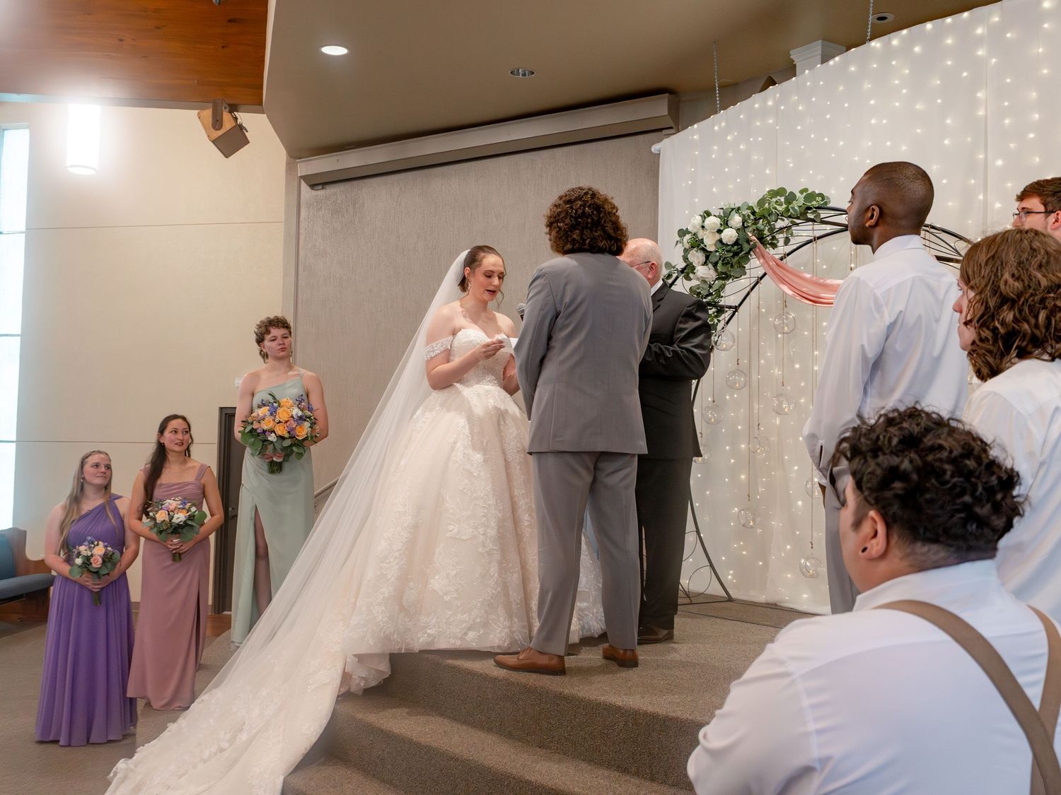 Church wedding ceremony with floral decorations and light backdrop.