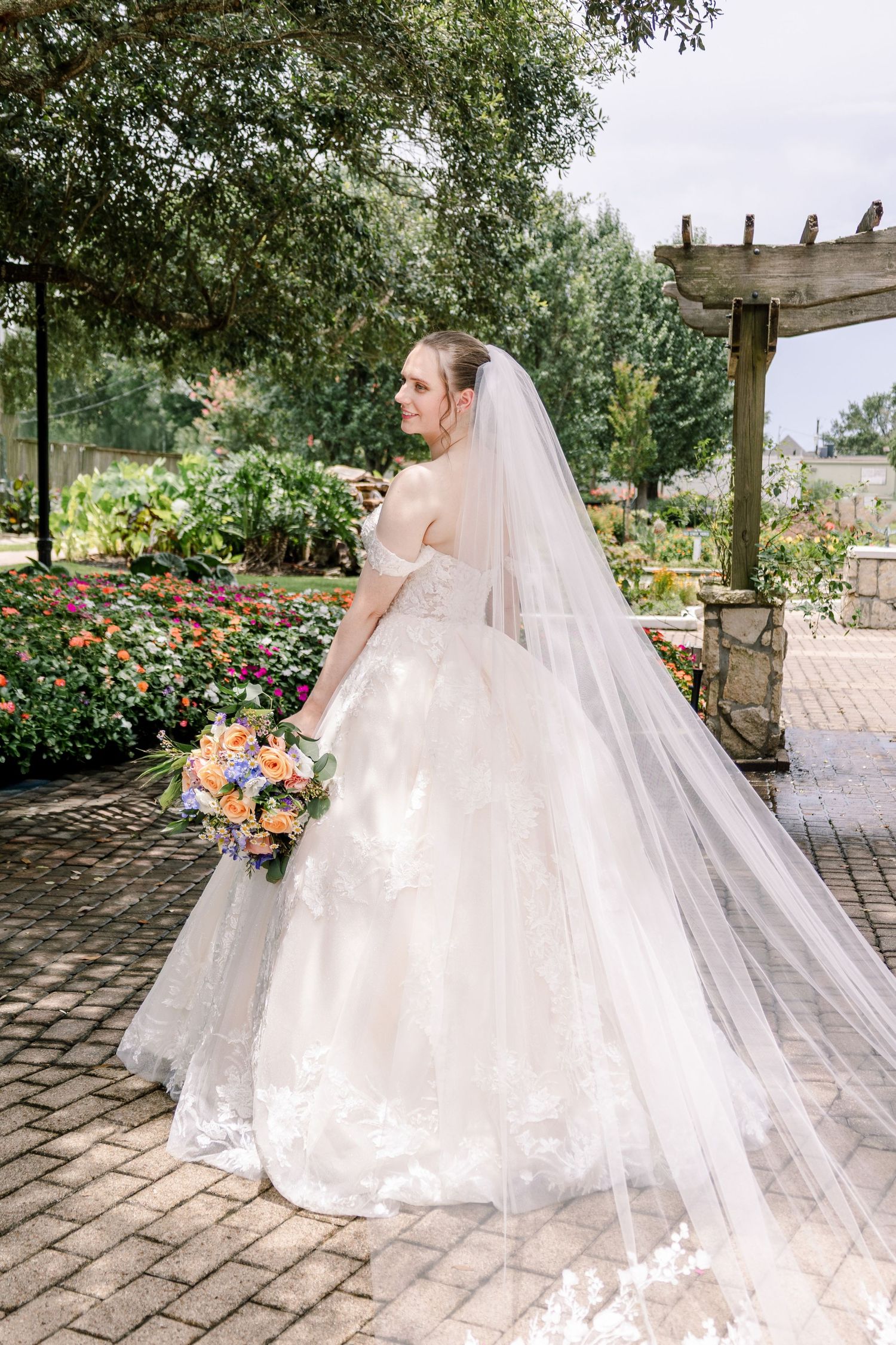 A stunning bridal portrait in a lace gown with cathedral veil against a garden backdrop.
