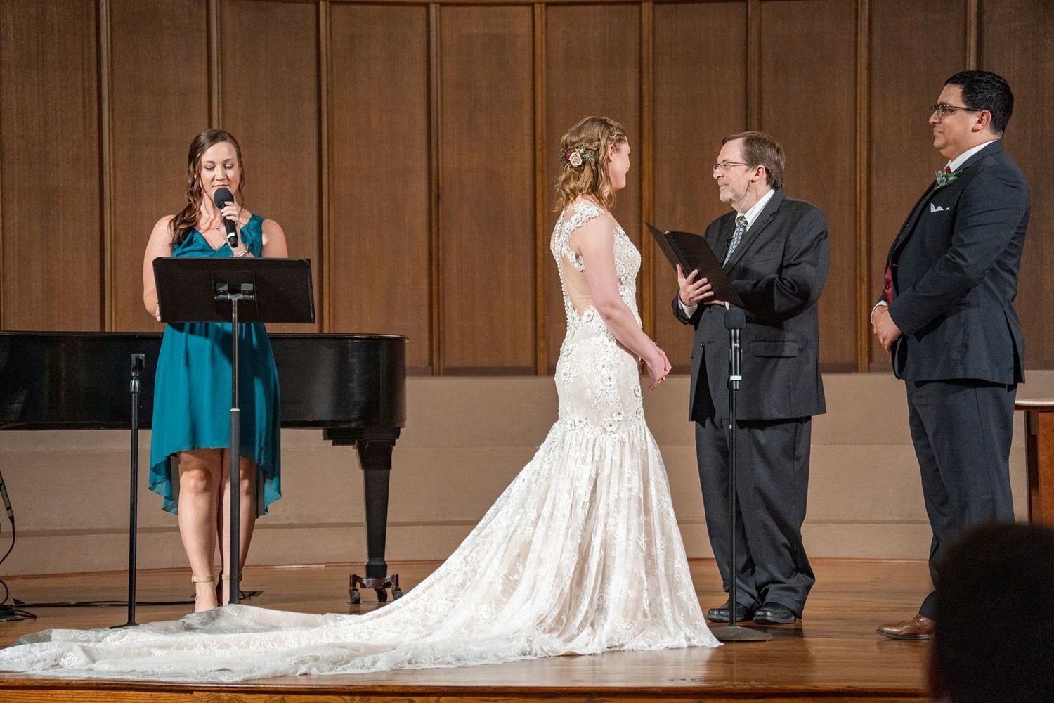 Singer performs at a wedding ceremony beside a grand piano as the bride and officiant stand nearby.