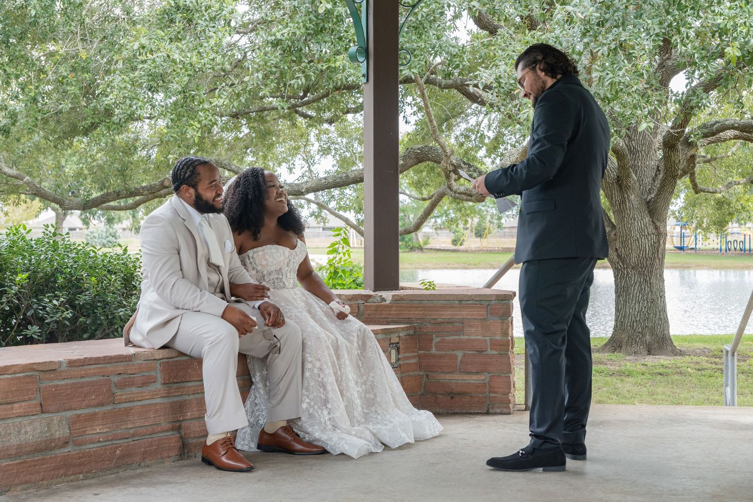 A couple in white attire share intimate moments on a brick wall under a covered patio.