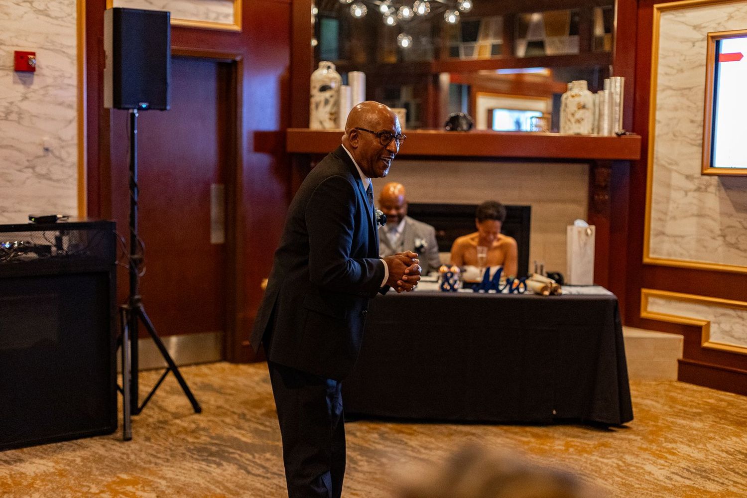 Man in dark suit standing at wedding reception near decorated table.