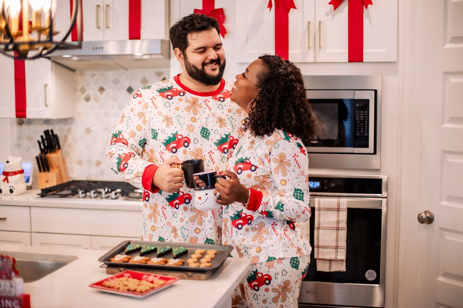 People in matching holiday pajamas prepare food and bake cookies together in a bright white kitchen.