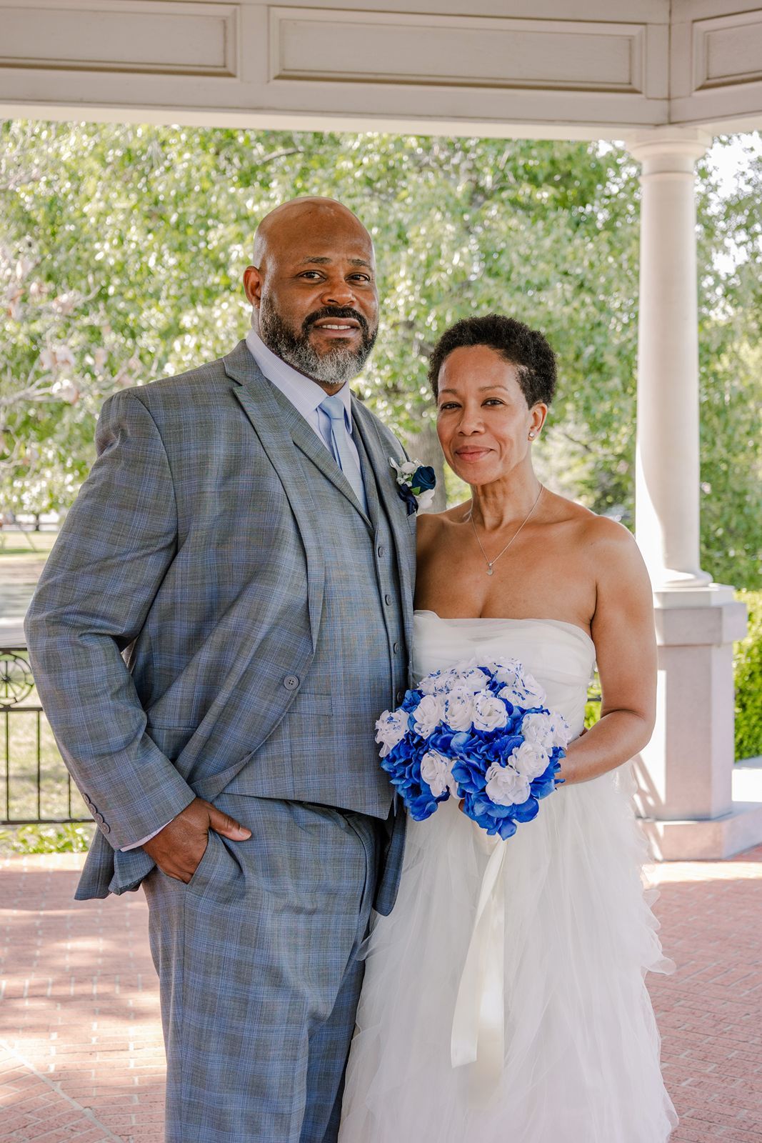 Bride and groom posing under a gazebo, bride holding blue and white bouquet.