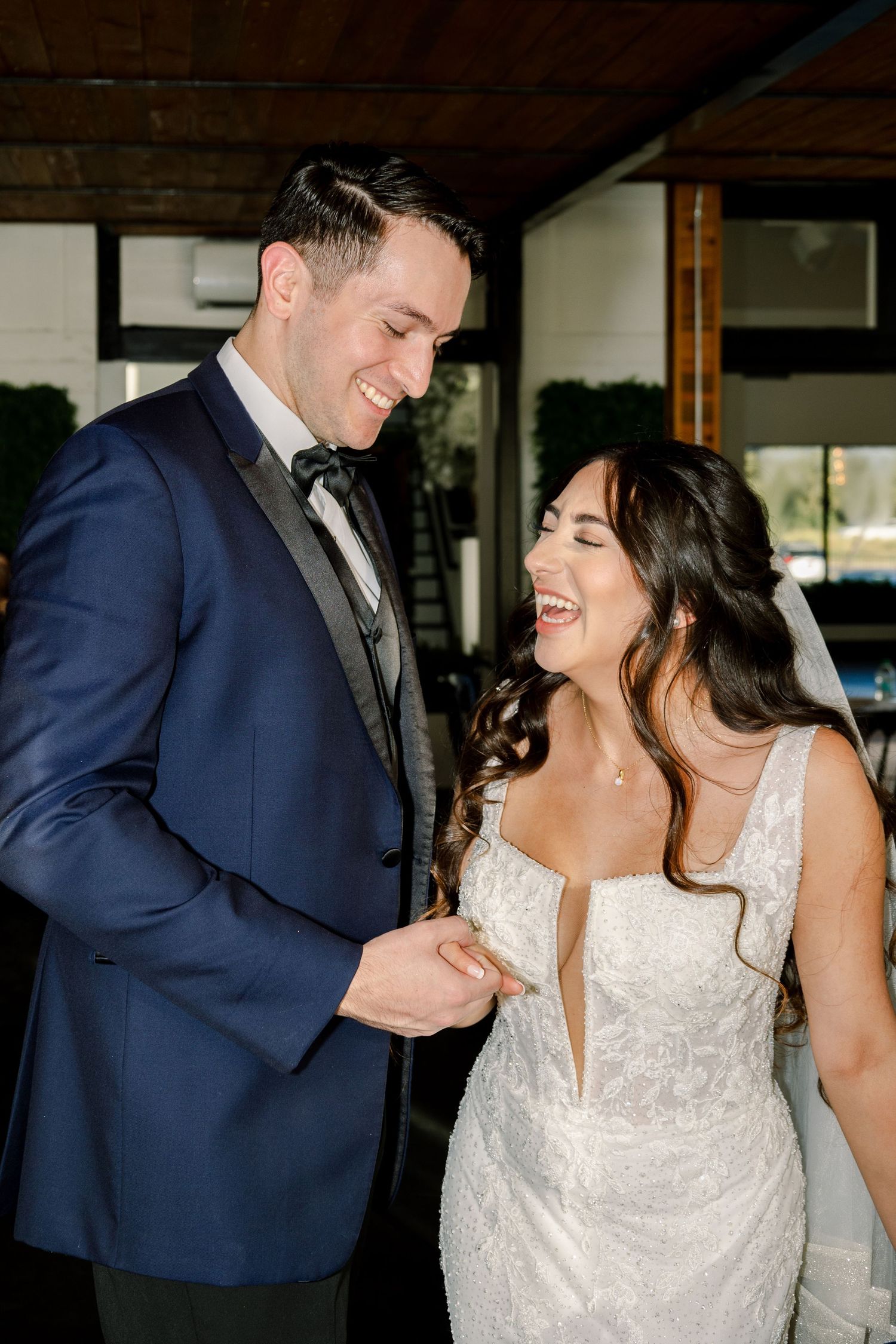 A happy couple shares a joyful moment together at their wedding, with the bride in white and groom in navy blue.