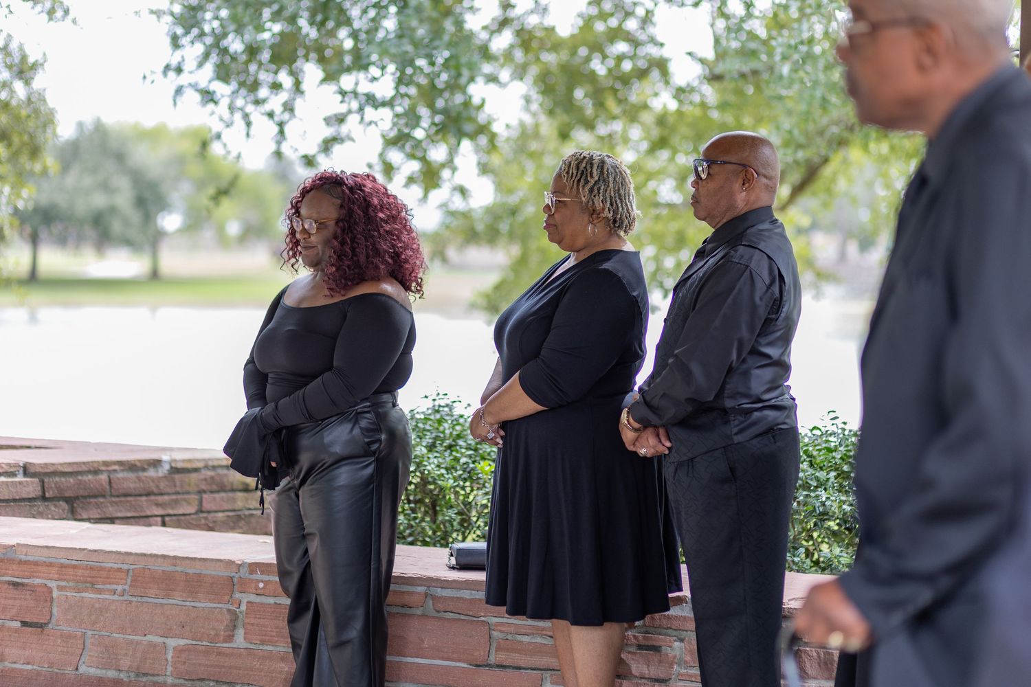 Wedding ceremony attendees in formal attire gathered near a brick wall outdoors.