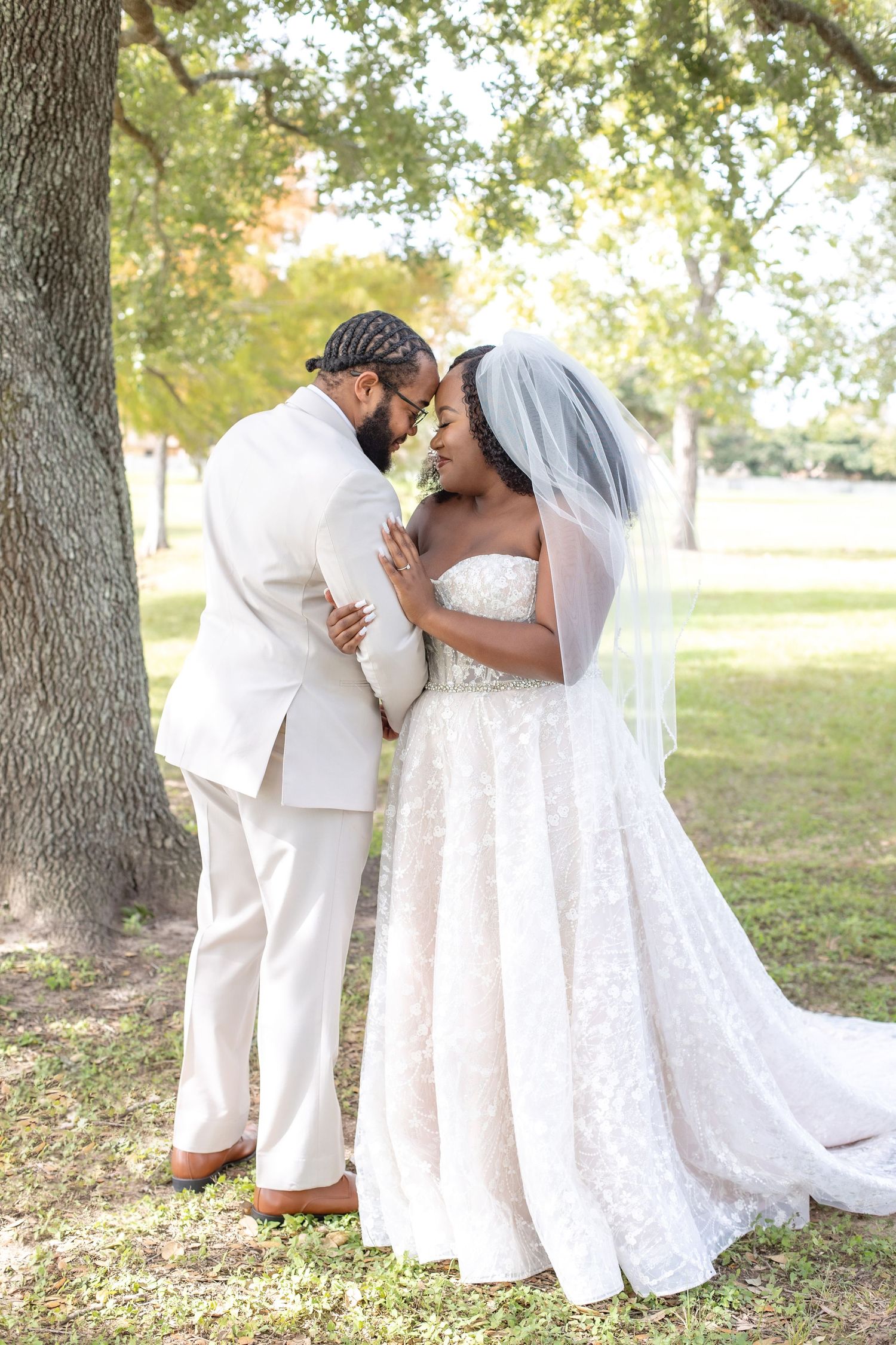 A romantic wedding photoshoot in a park setting with the couple in elegant white attire embracing.