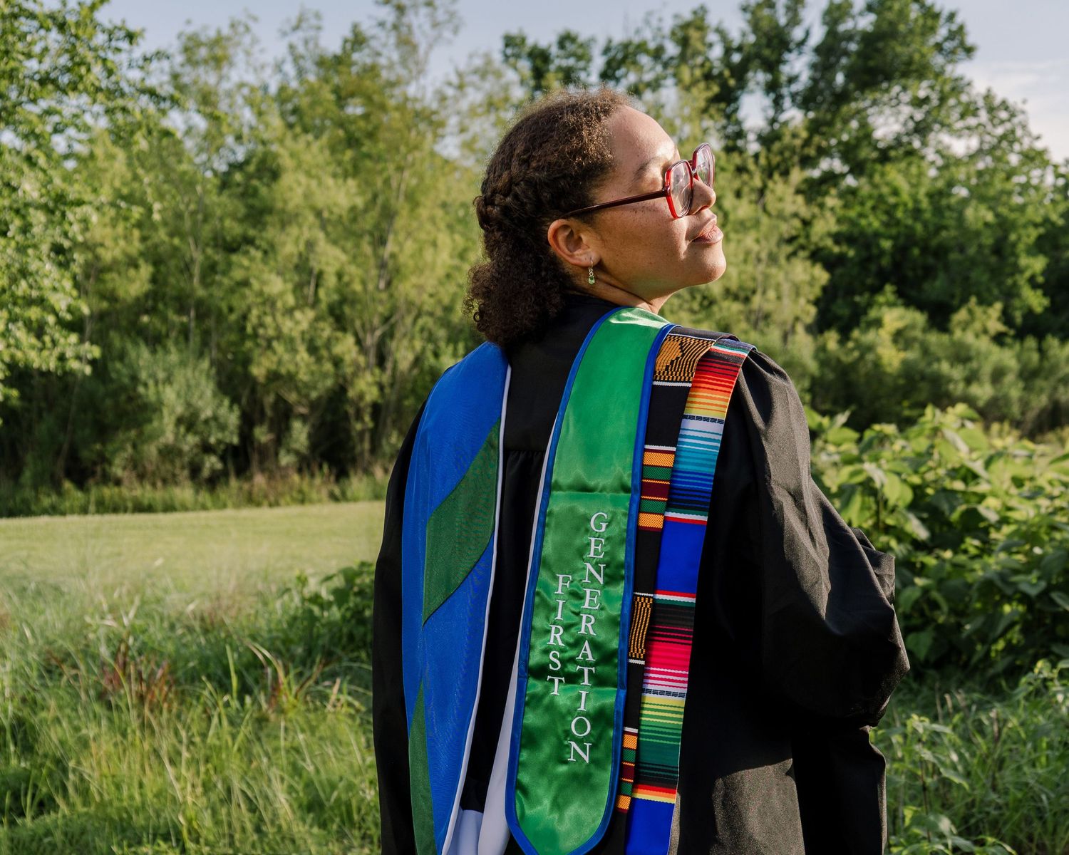 Person wearing colorful religious stoles and garments outdoors against greenery.