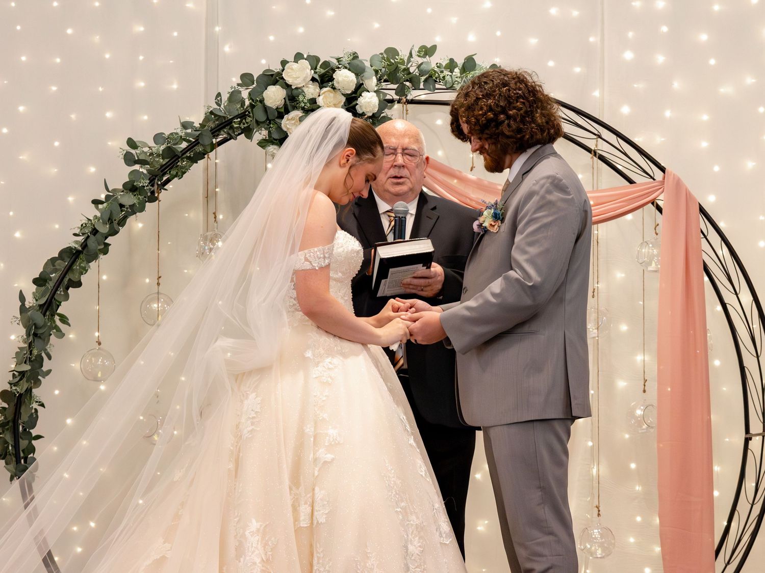 A romantic wedding ceremony moment beneath a decorated arch with twinkling lights.