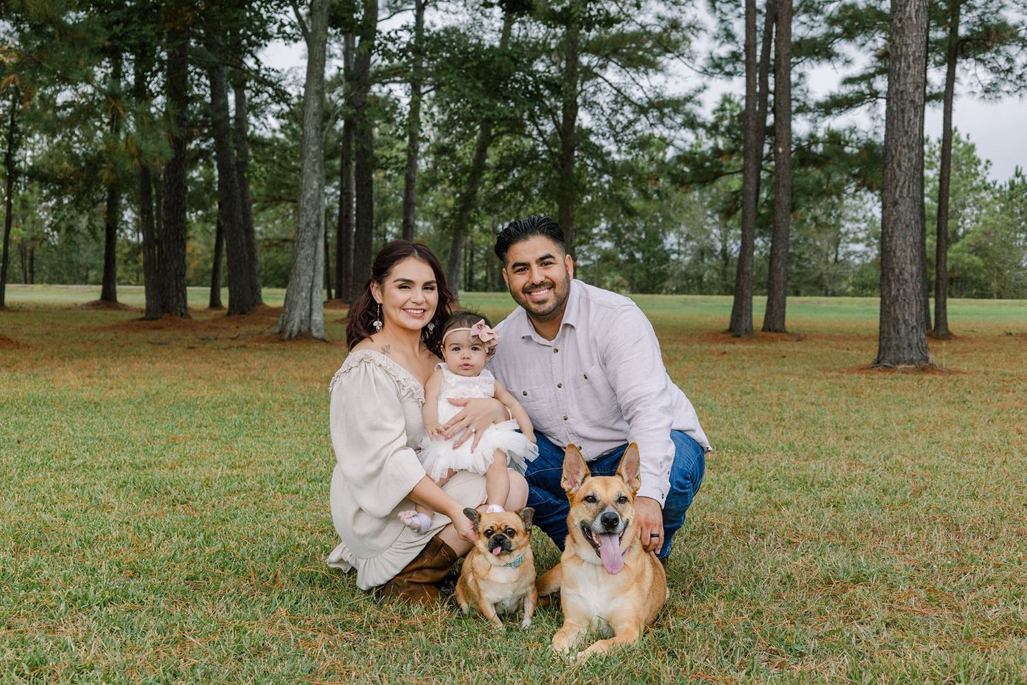A happy family poses outdoors with their two dogs in a grassy park setting.