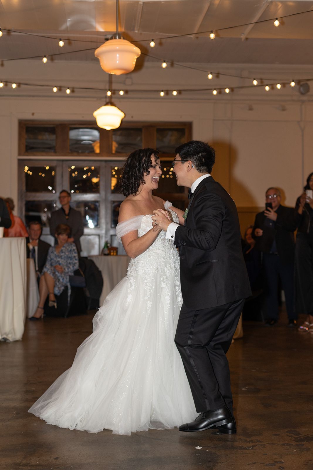Couple dancing together at a wedding reception in a venue decorated with string lights and lanterns.