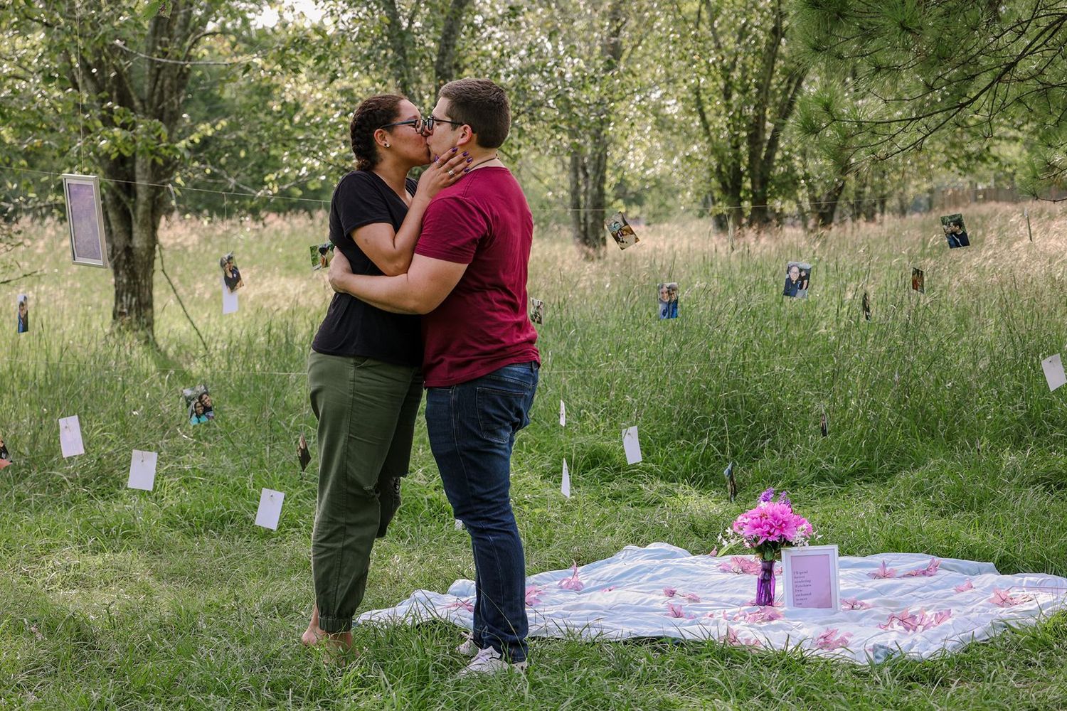 Couple sharing a romantic kiss during an outdoor picnic proposal in a lush green meadow with wildflowers.
