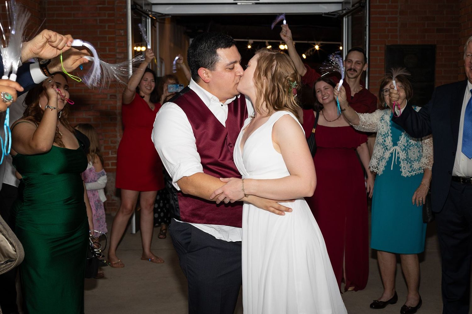 Bride and groom share a kiss during their wedding reception while guests celebrate around them.