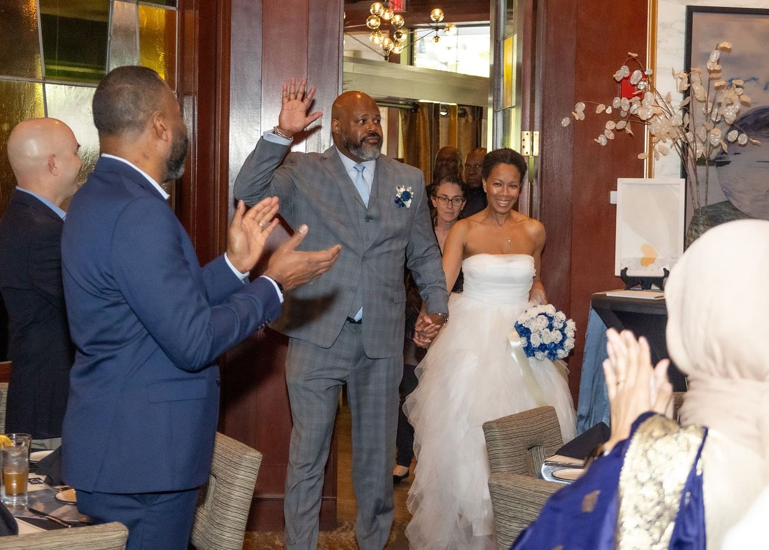 Wedding guests dancing and celebrating at a reception in a warmly lit indoor venue.