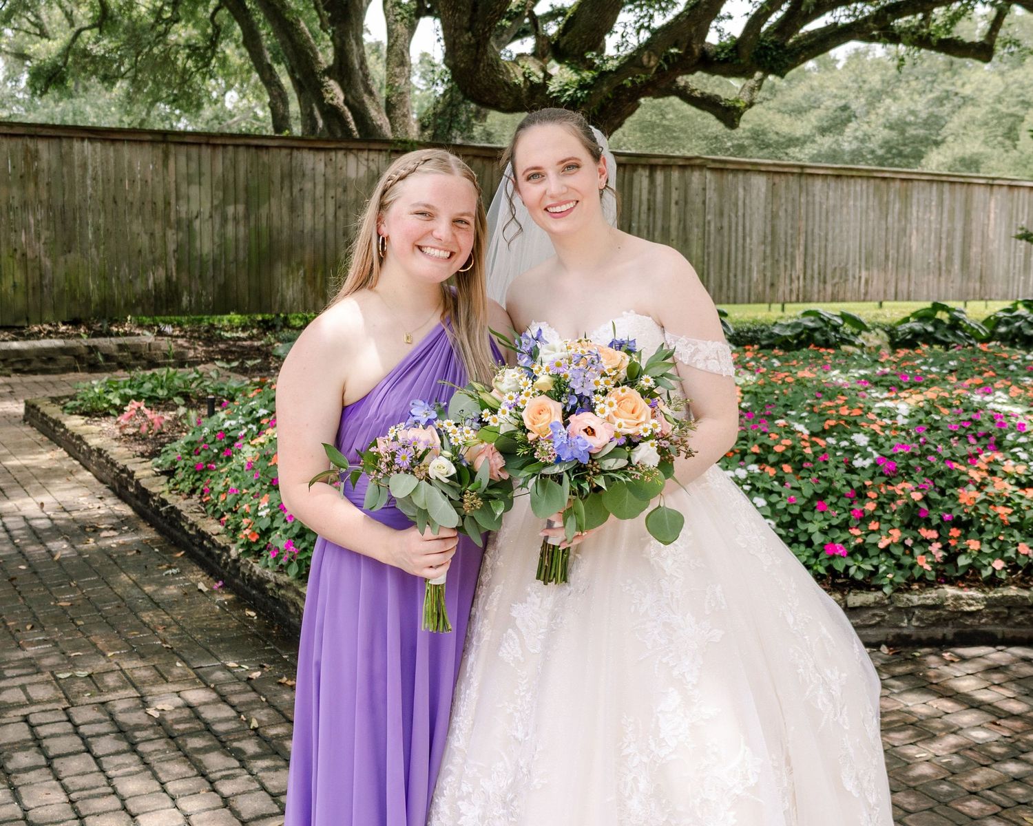 Wedding party in purple dresses and white gown posing in a lush garden setting.