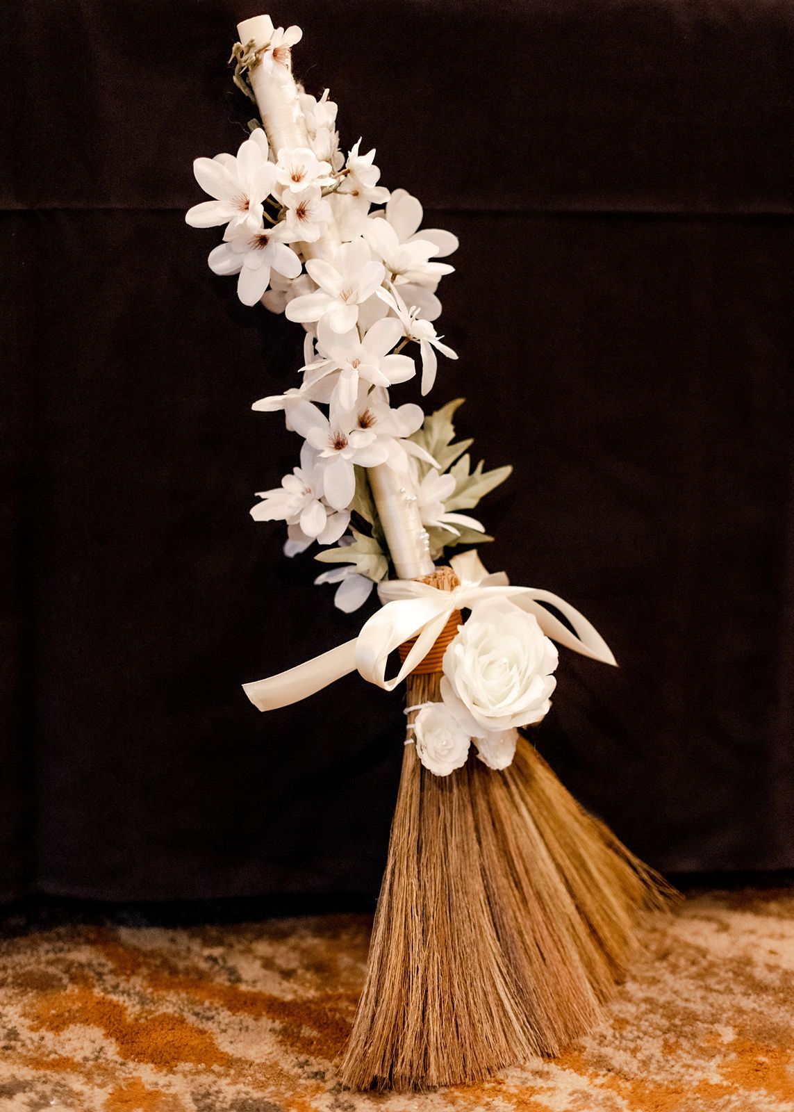 Decorated wedding jumping broom with white flowers, ribbon, and a rose for a traditional ceremony.