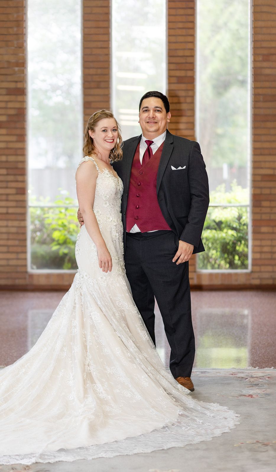 A couple poses together in formal wedding attire with a flowing white dress and black suit in an elegant indoor setting.