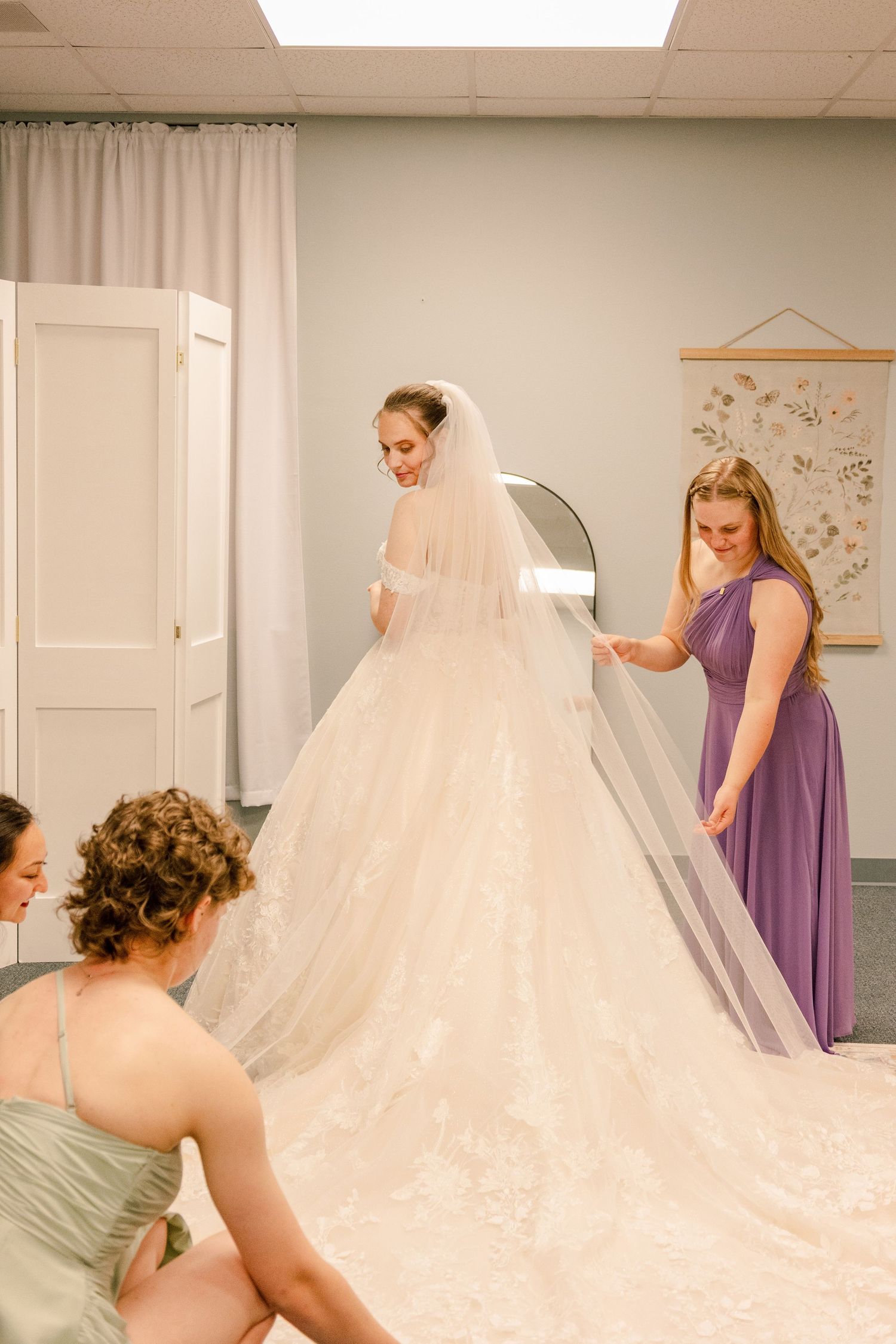 Bridesmaids in purple and pink dresses help style the bride's elaborate wedding gown train.