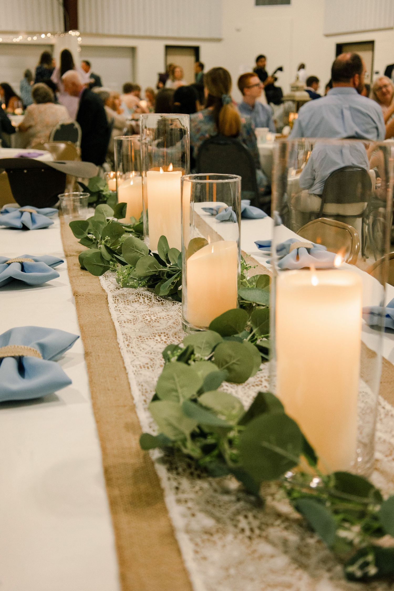 Elegant table setting with lit candles and greenery garland running down a burlap table runner.