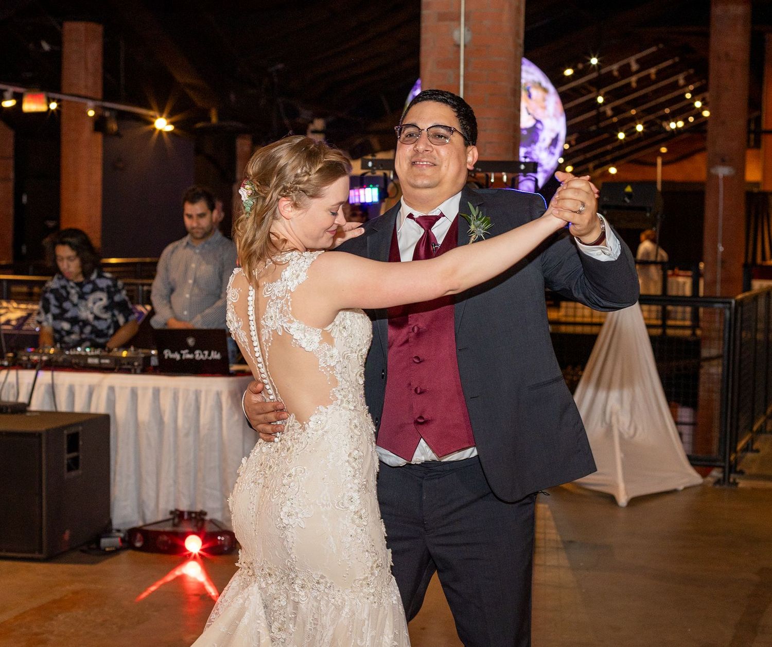 Bride and groom share their first dance at a romantic wedding reception with warm string lights.