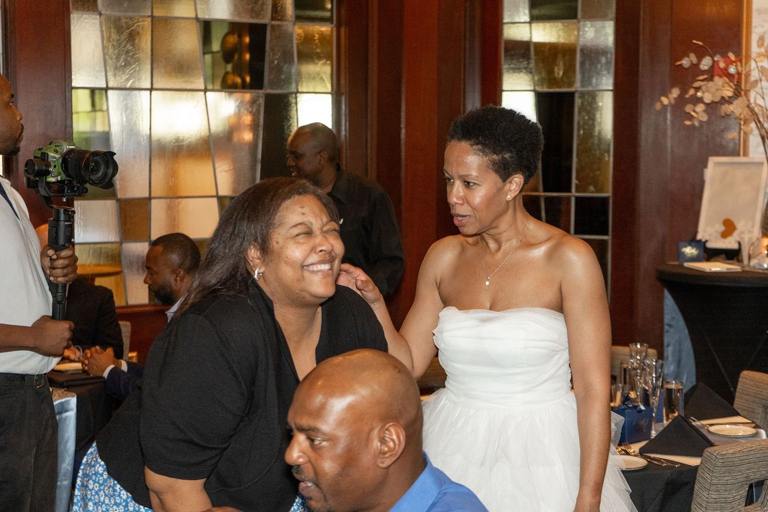 Bride in white strapless gown smiles with guests at wedding reception.
