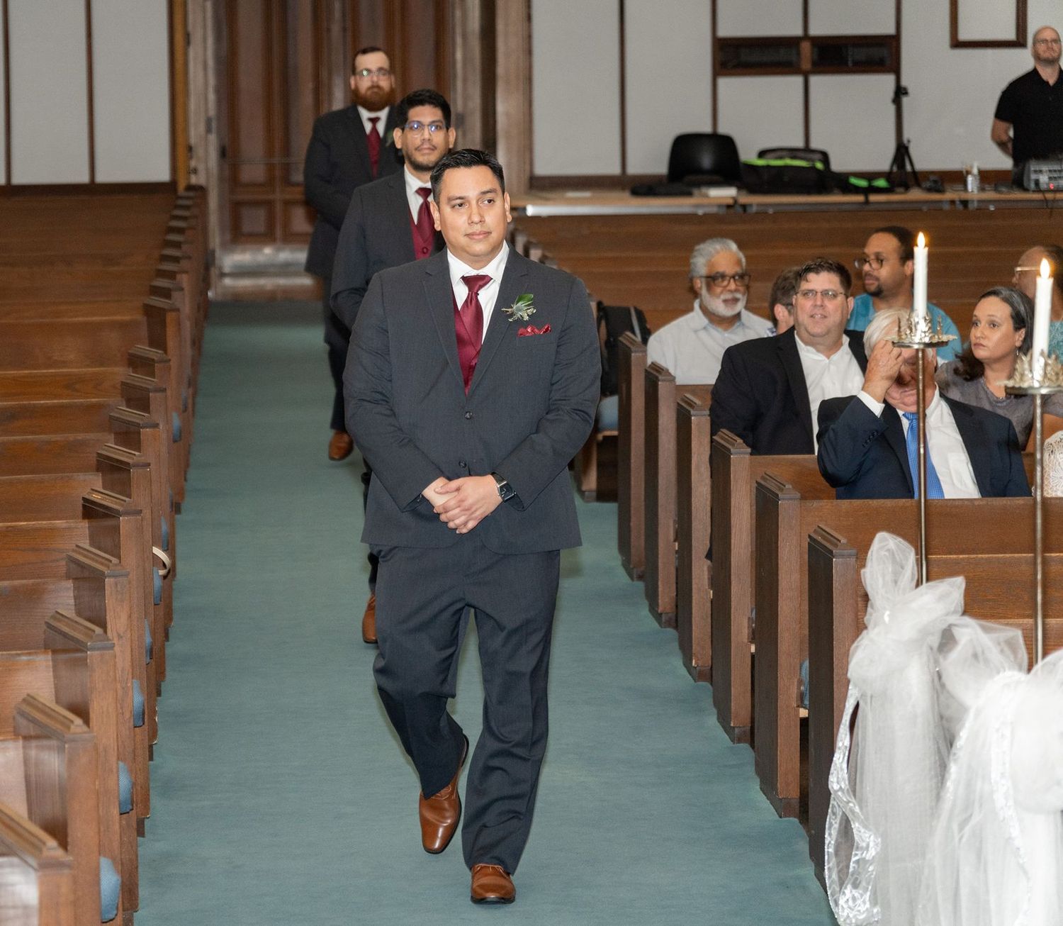 Groomsmen walking down church aisle in navy suits during wedding ceremony procession.