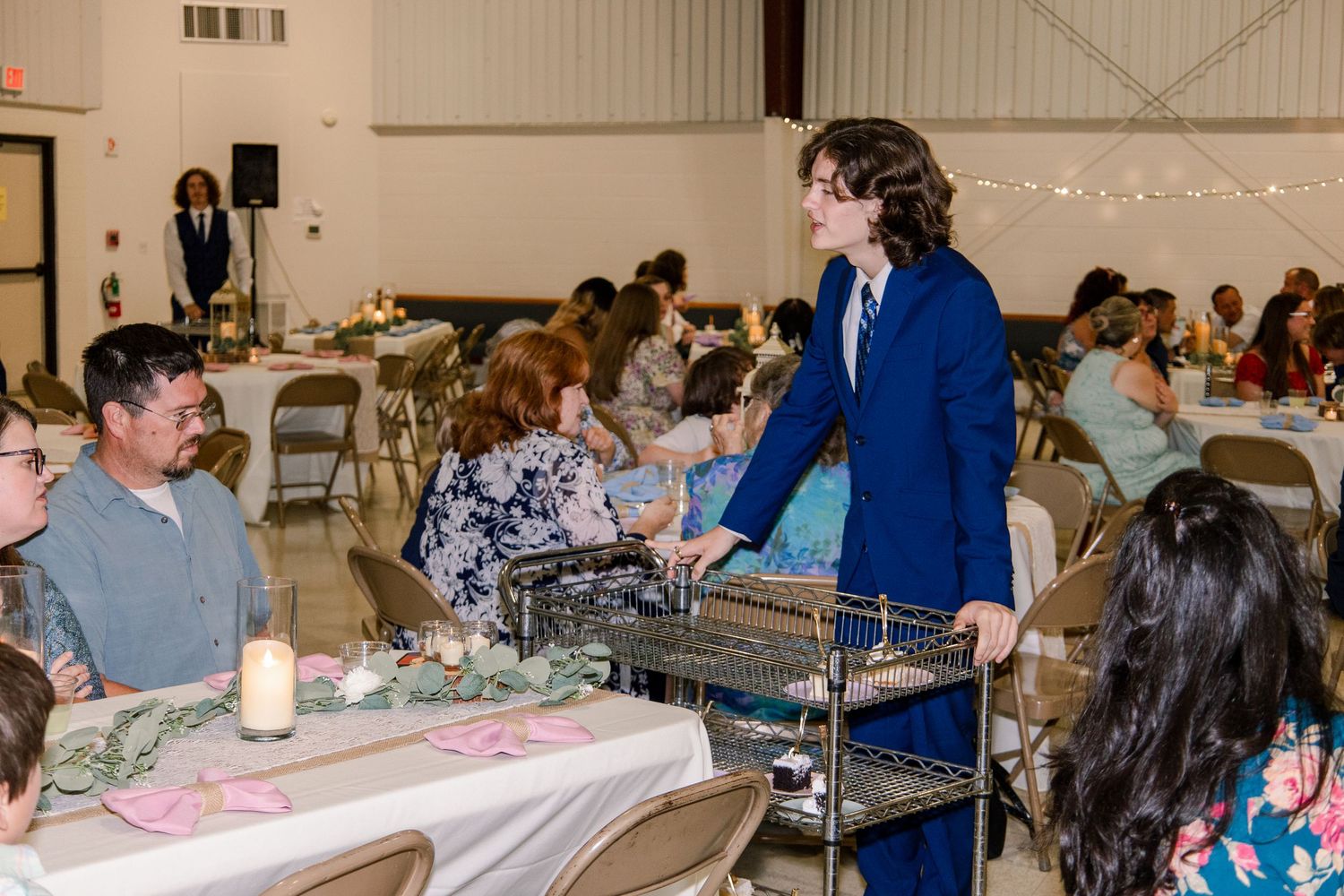Wedding reception with guests being served food from a catering cart in a decorated banquet space.
