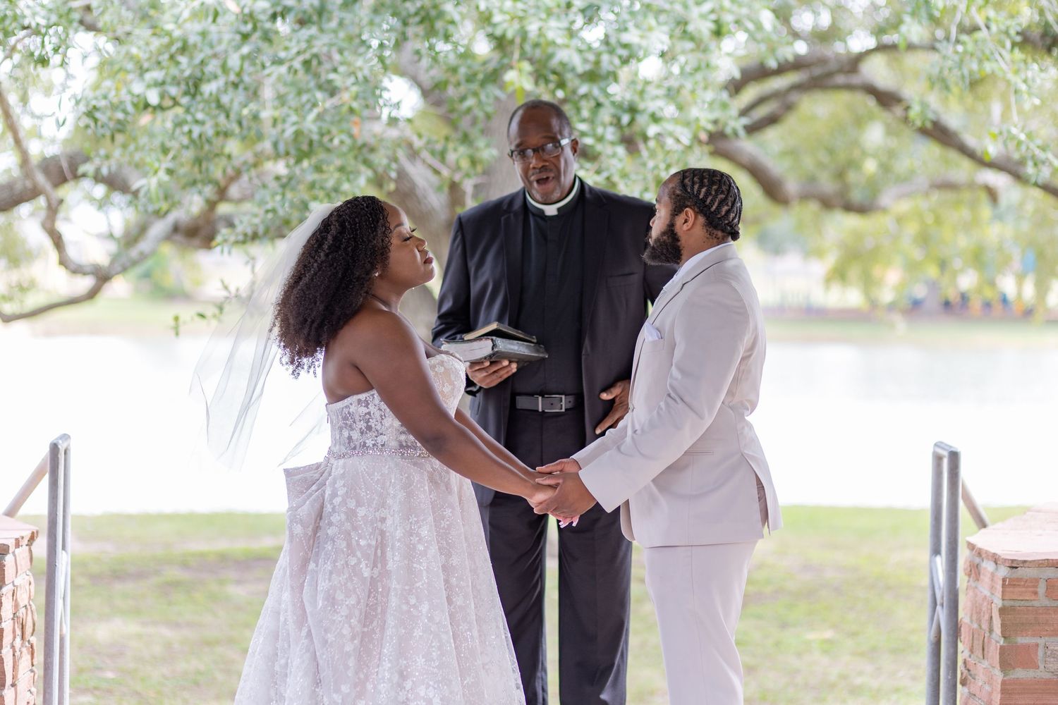 A wedding ceremony taking place under a gazebo with a waterfront backdrop.
