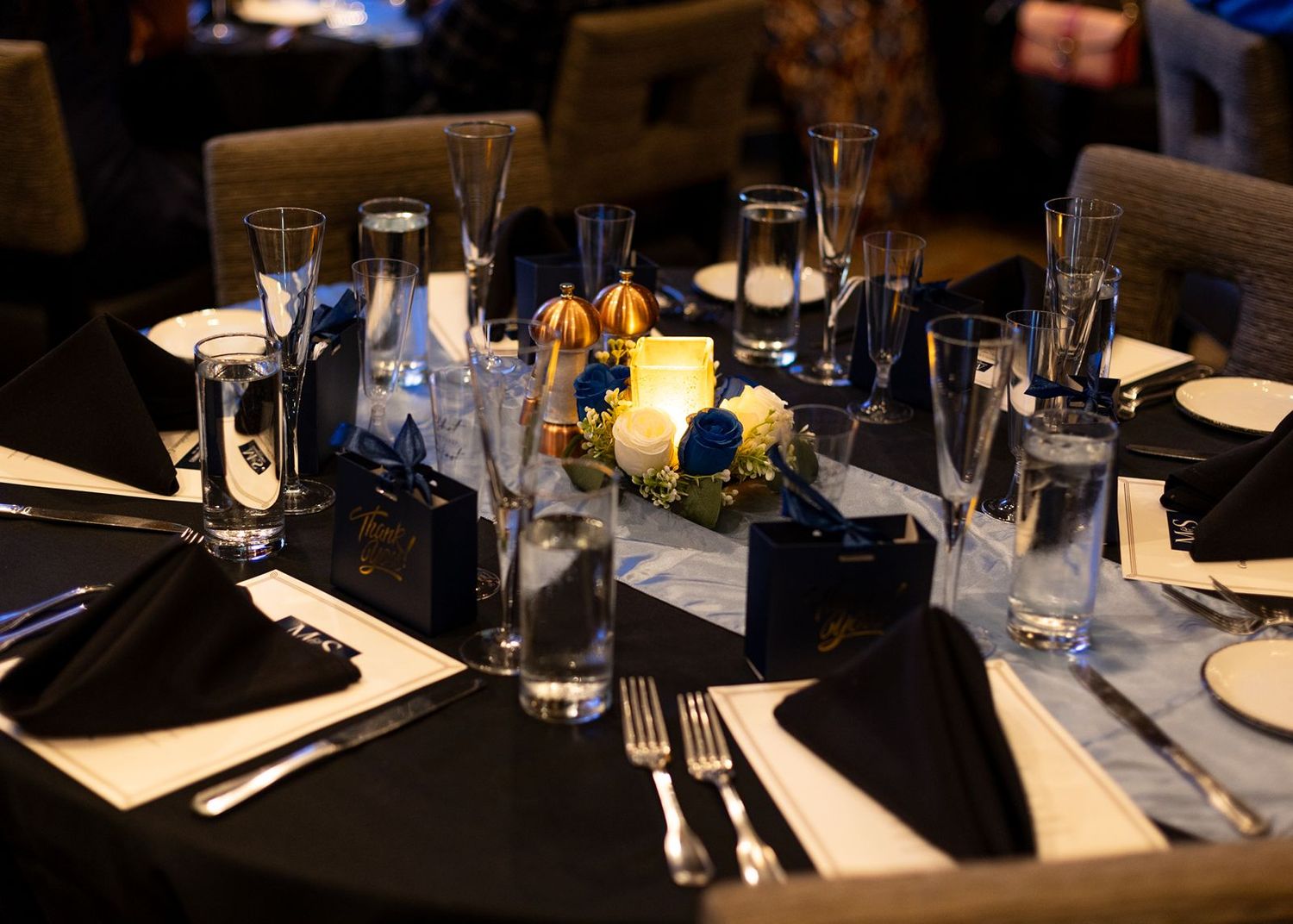 Elegant wedding reception table set with black linens, floral centerpiece, candles, and glassware.
