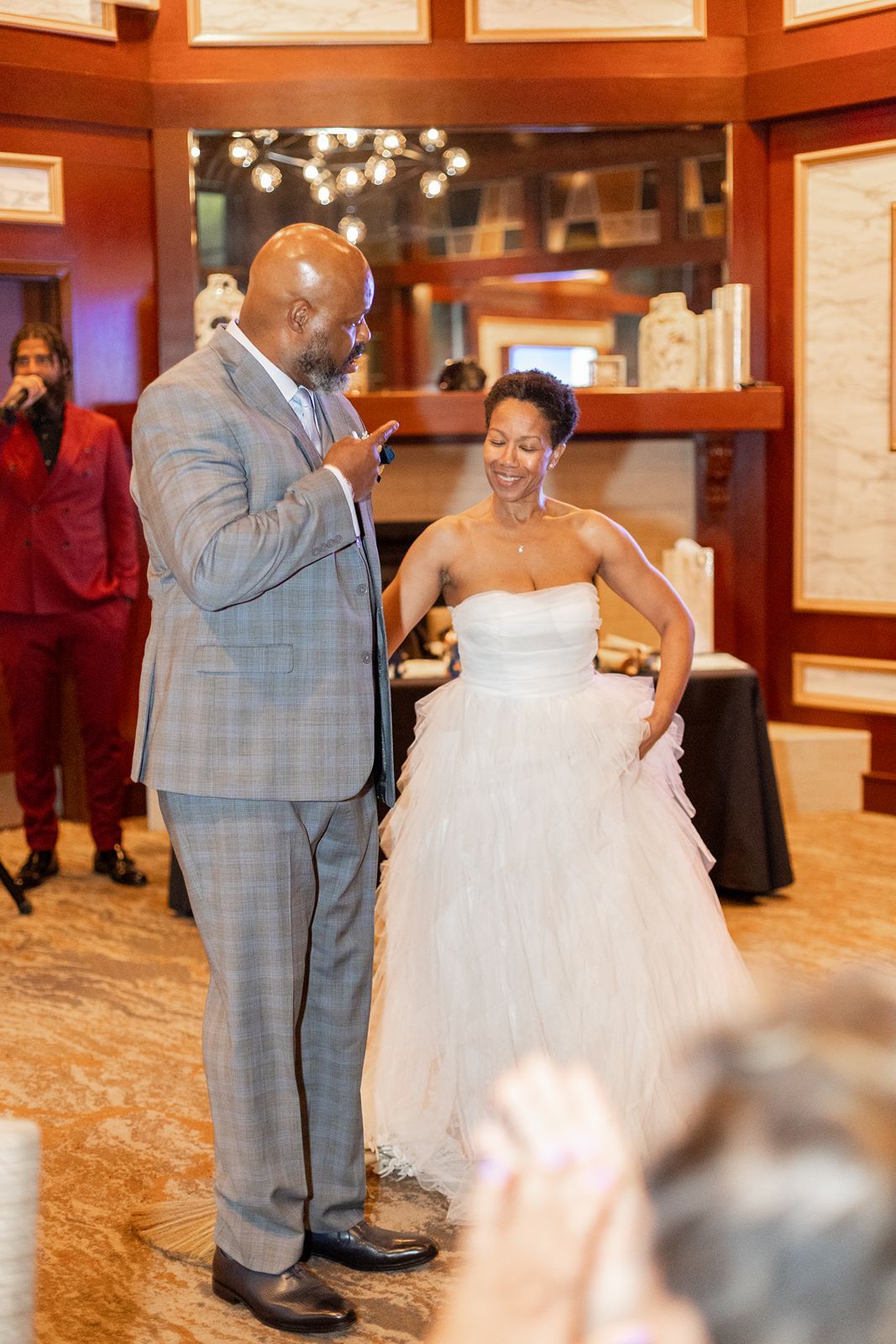 Bride in strapless white tulle gown laughing with groom in gray plaid suit during wedding reception.