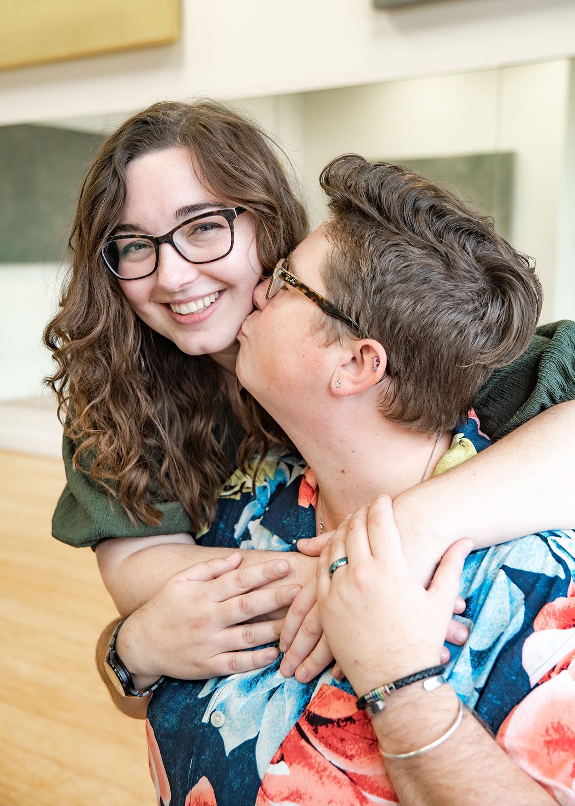 A couple embraces and shares a joyful moment together, with one wearing glasses and a floral patterned outfit.