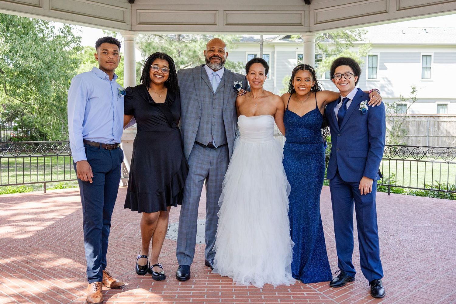 Family group photo at a wedding with bride in white gown and guests in formal attire outdoors.