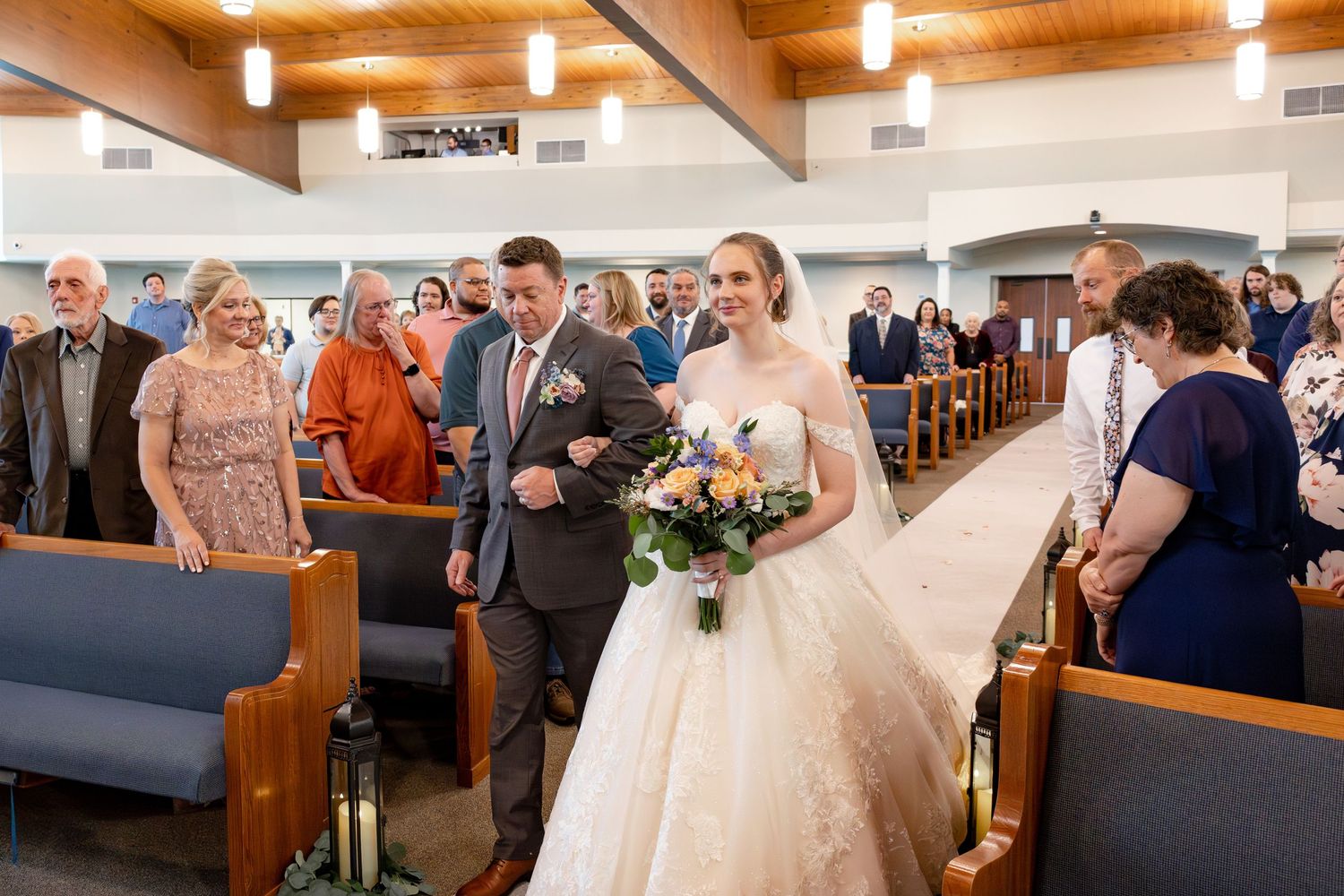 Wedding party processional in a modern church with exposed beam ceiling and pendant lights.