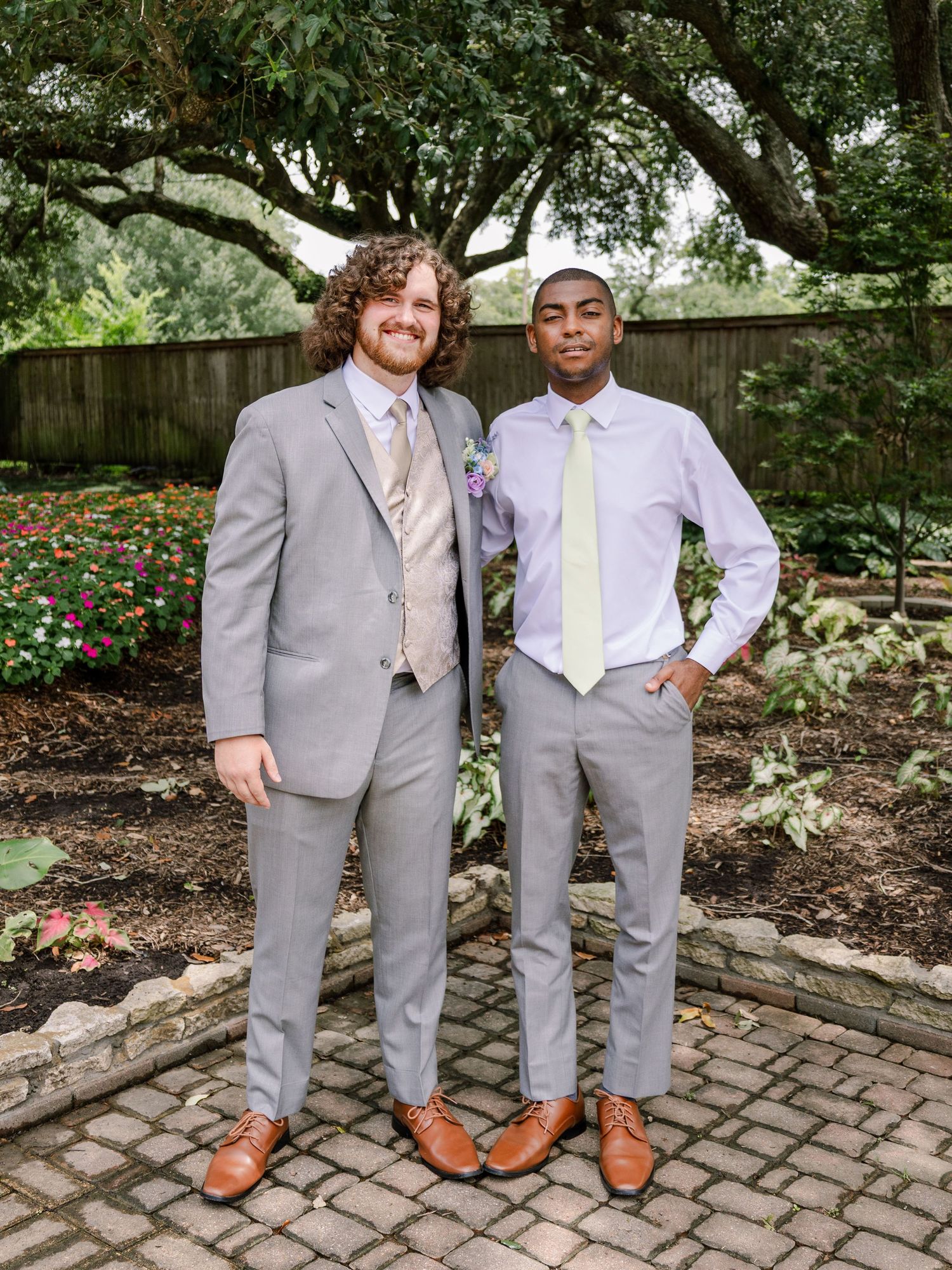 Wedding party members in coordinated gray suits standing together on a brick pathway.