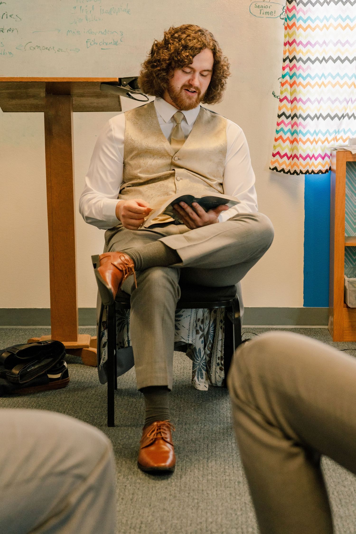 Person in formal attire reading while seated in a chair.