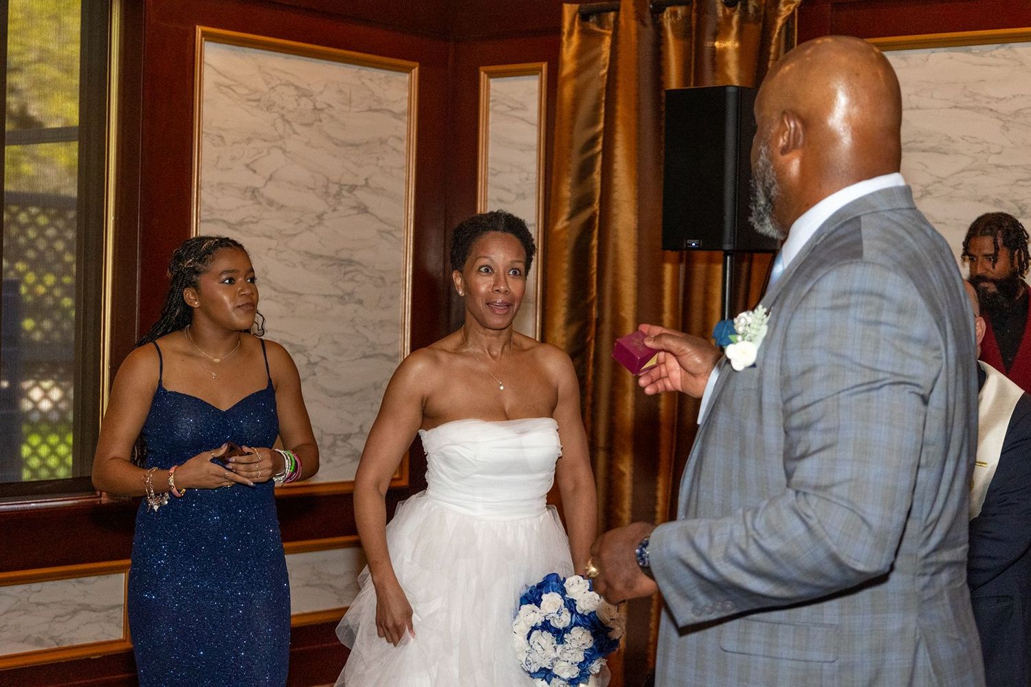 Bride in white gown holds bouquet while chatting with guests at elegant wedding reception.