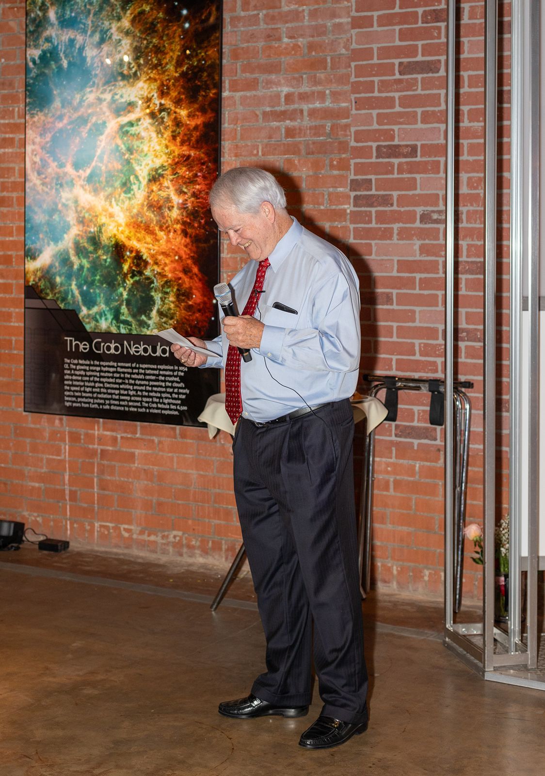 Elderly man in blue shirt and red tie standing near Crab Nebula exhibit.
