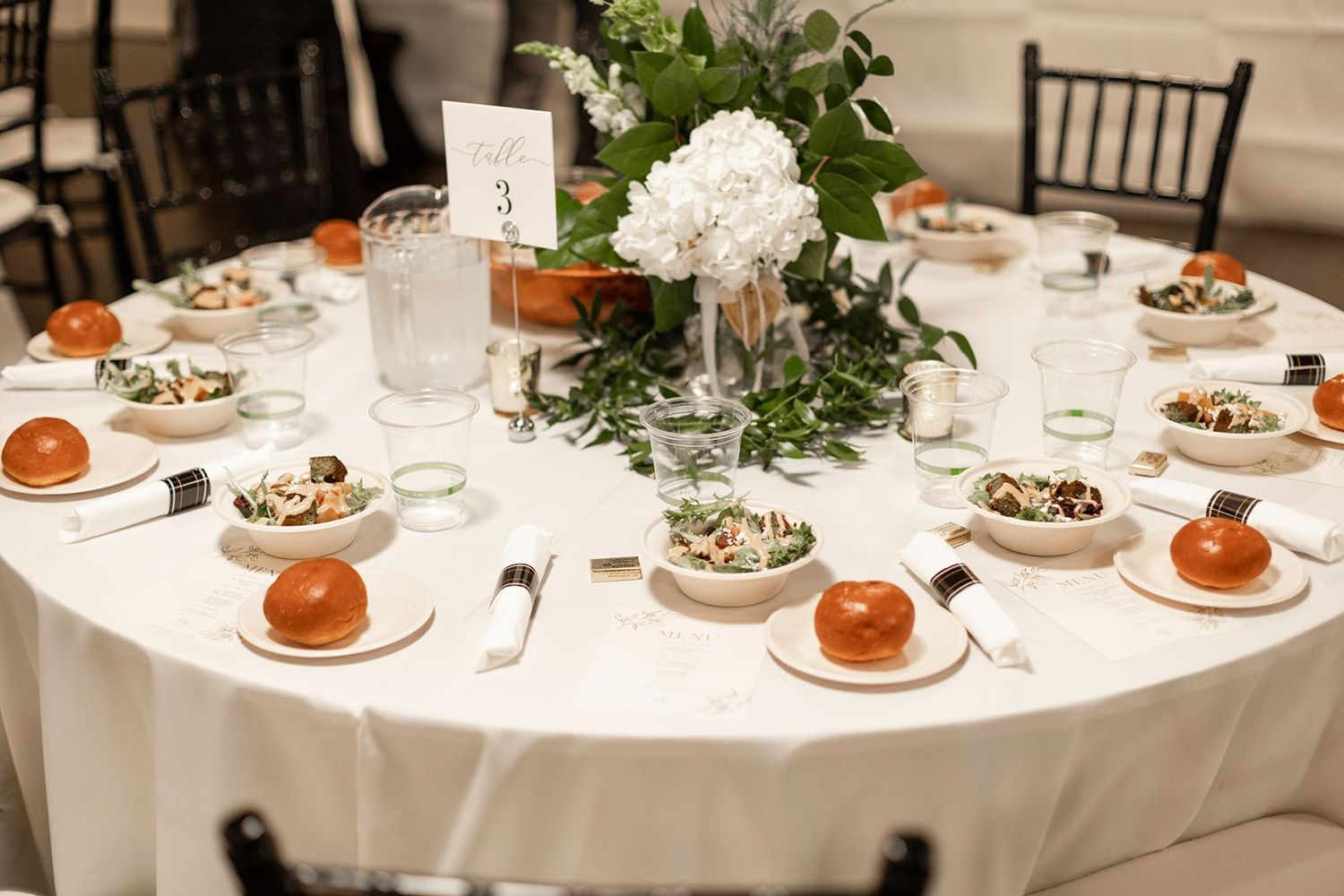 Elegant wedding reception tables set with white linens, floral centerpieces, and place settings in a formal dining room.