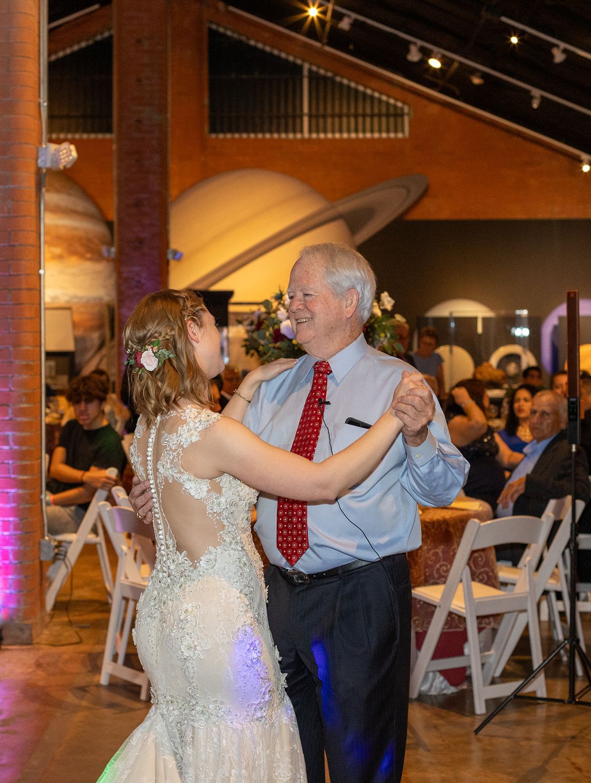 Bride in lace gown shares father-daughter dance at wedding with planet decor.