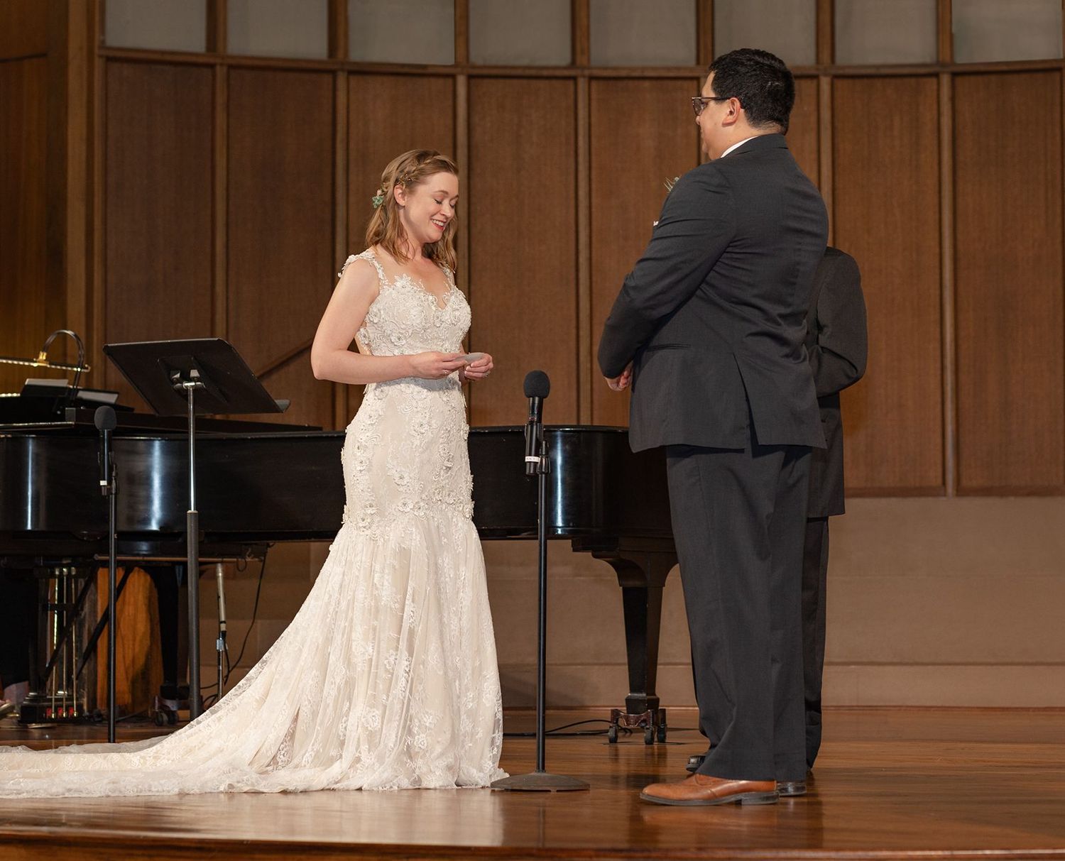 Bride and groom exchange vows on a wooden stage with a grand piano during their wedding ceremony.