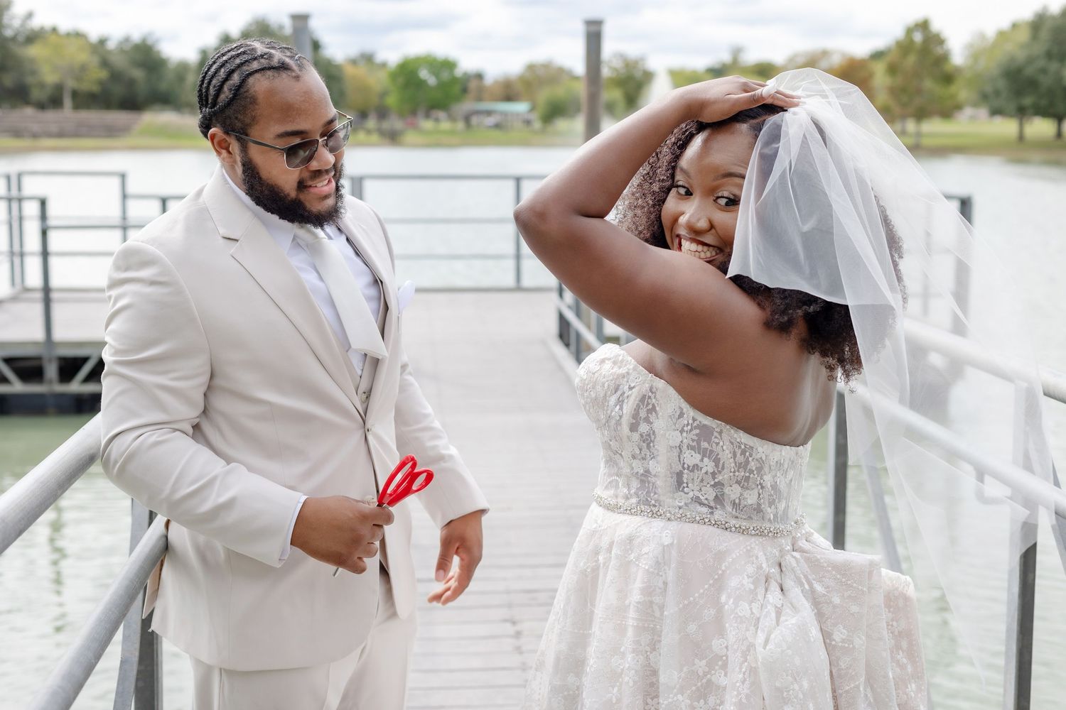 A couple in white wedding attire laughs together during a joyous outdoor photo session on a bright day.