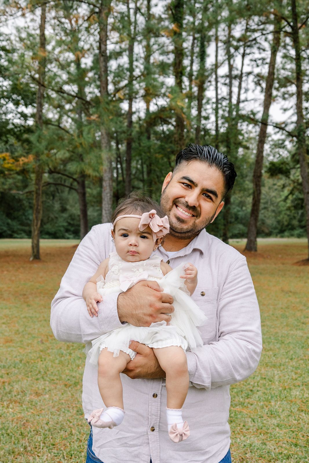 A loving moment captured in nature with pine trees in the background on a grassy field.